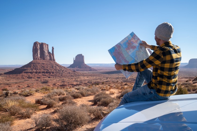 Young man outside car looking at road map for directions exploring national parks and nature ready for adventure