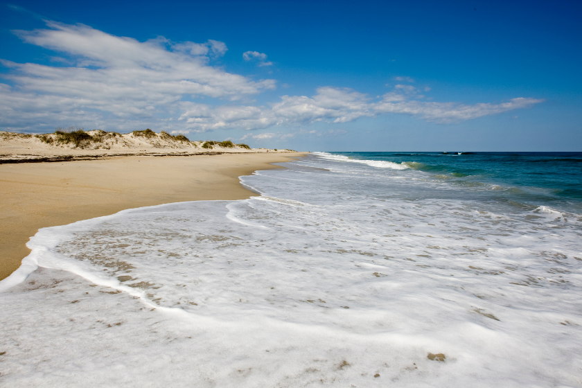 Ocean waves roll over stretching to the horizon beach leaving white foam that sparkles in the sun light.