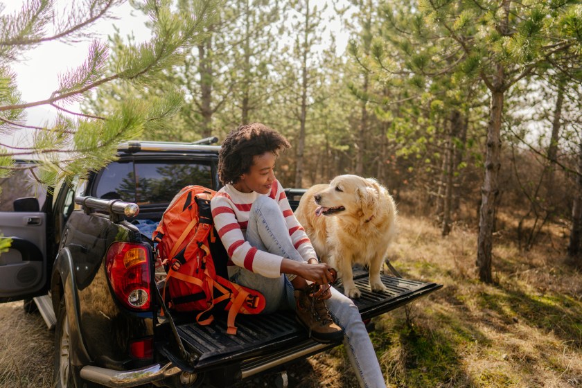 Photo of young smiling woman on a road trip with her best friend, her retriever dog, riding along on their pick up truck
