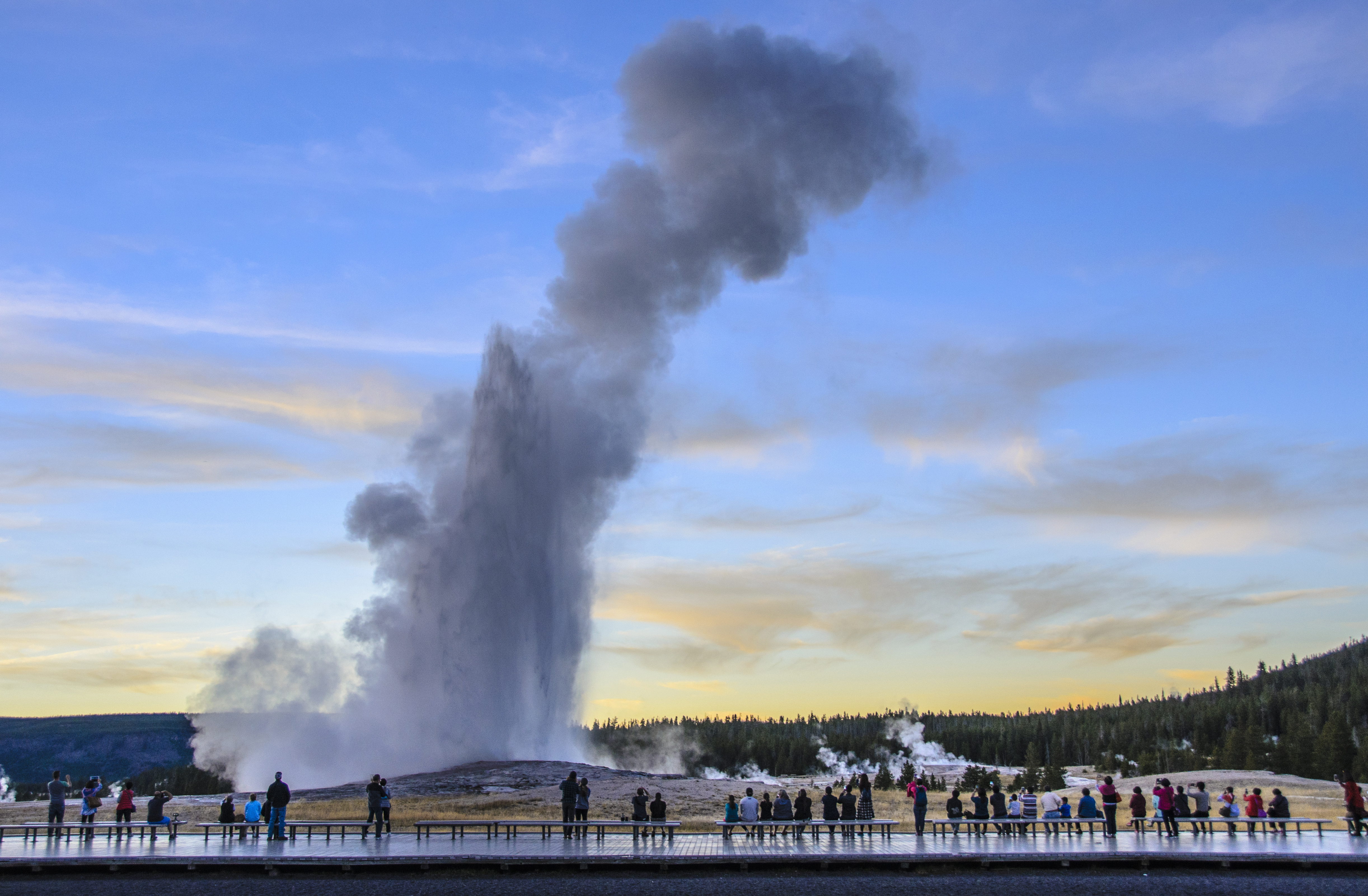 Groups of people have been waiting to watch, experience and photograph this Old Faithful eruption just after sunset on a sunny early autumn day.