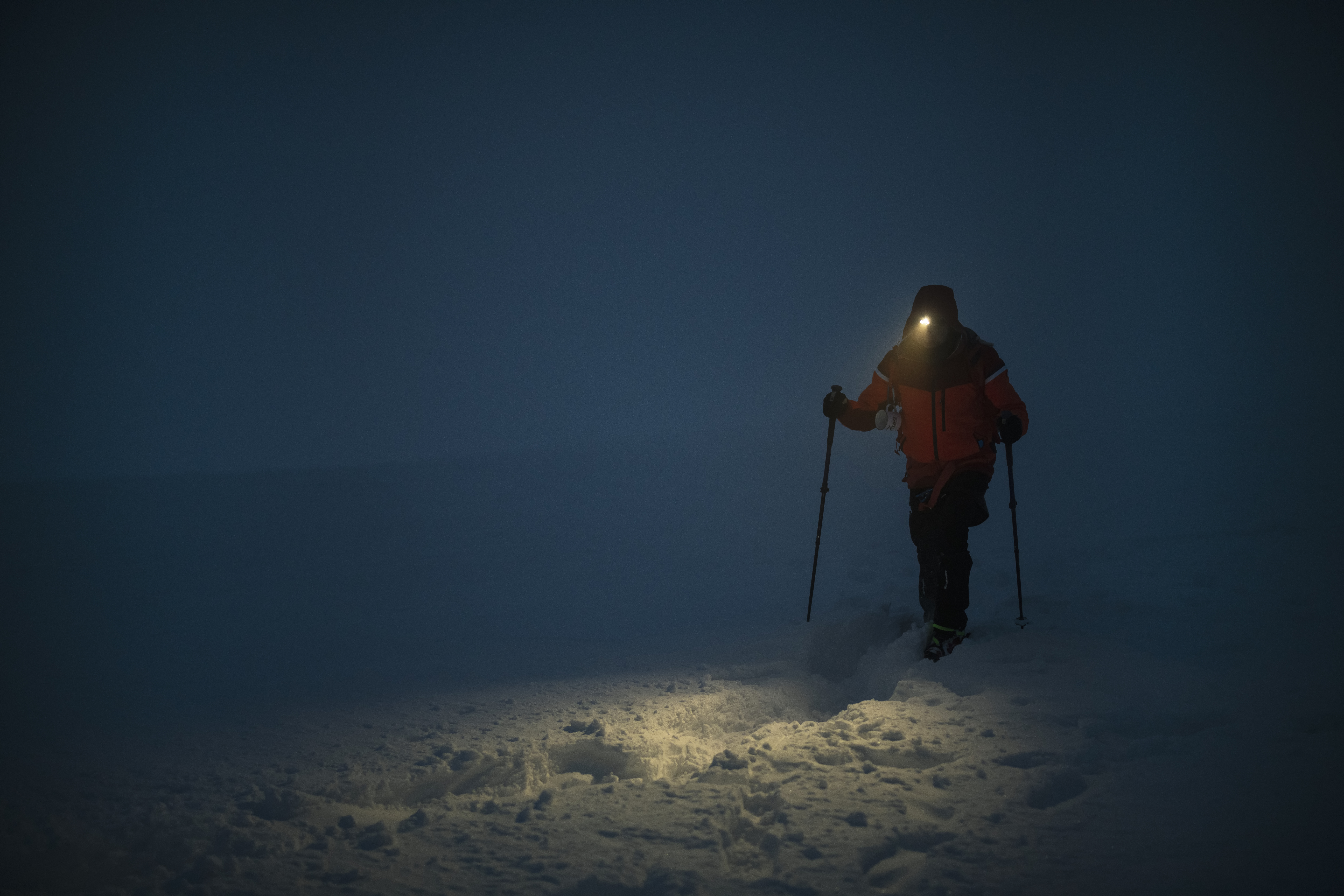 Cross country skiier wearing a headlight on a dark snowy trail.