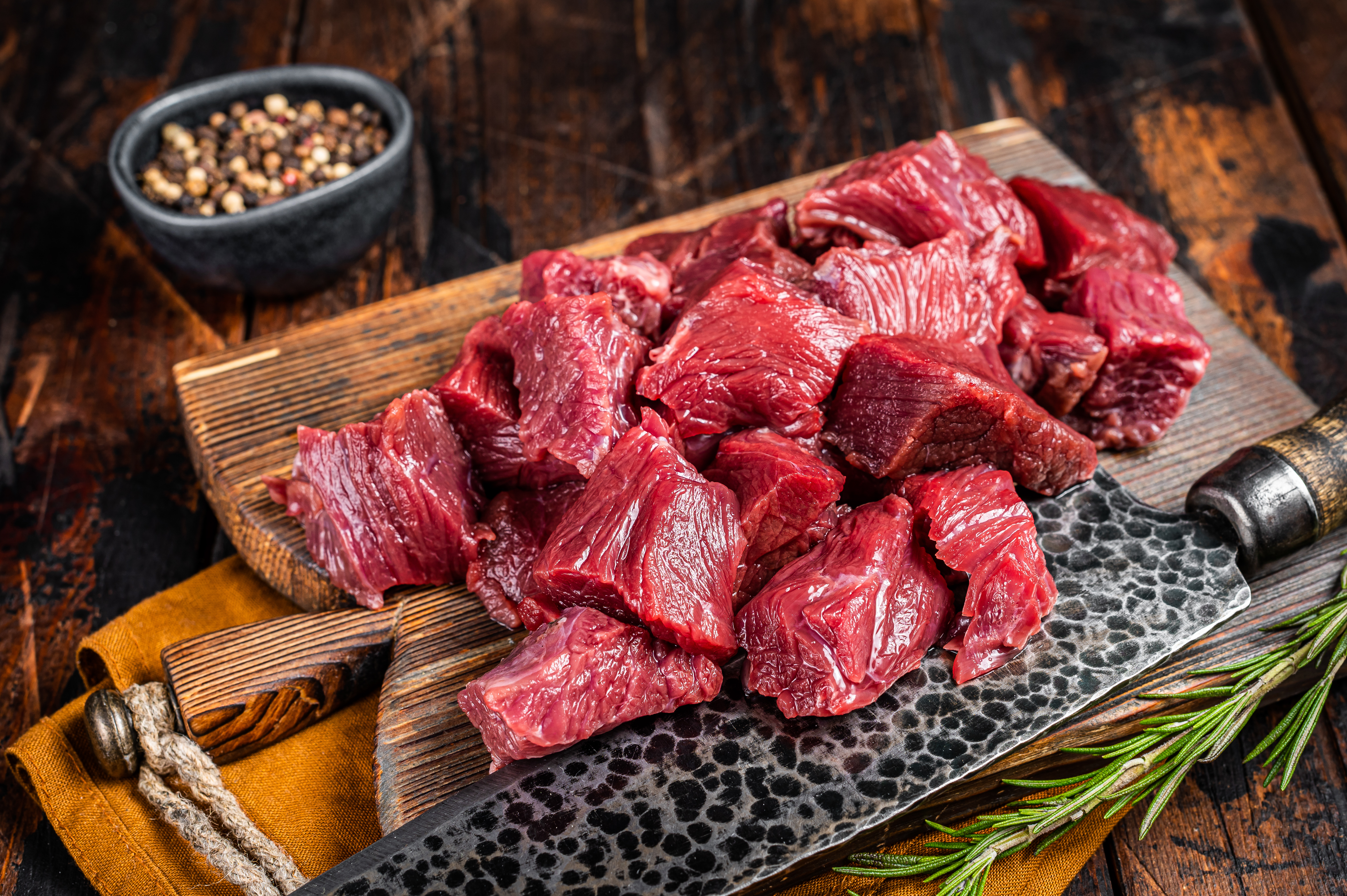 Sliced Raw venison dear meat for a stew, game meat on butcher cutting board. Wooden background. Top view.