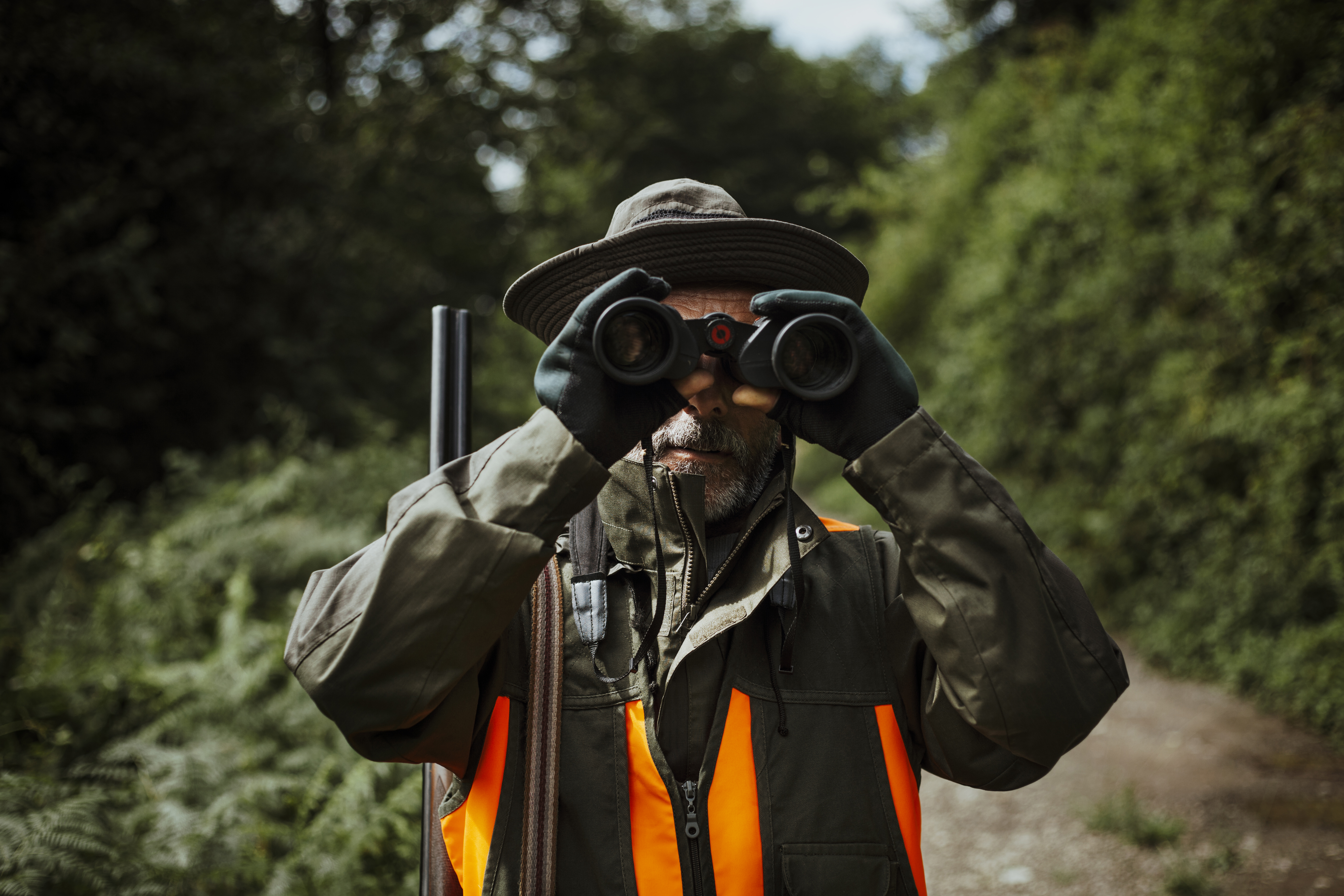 Hunter with rifle on shoulder checking terrain with binoculars.