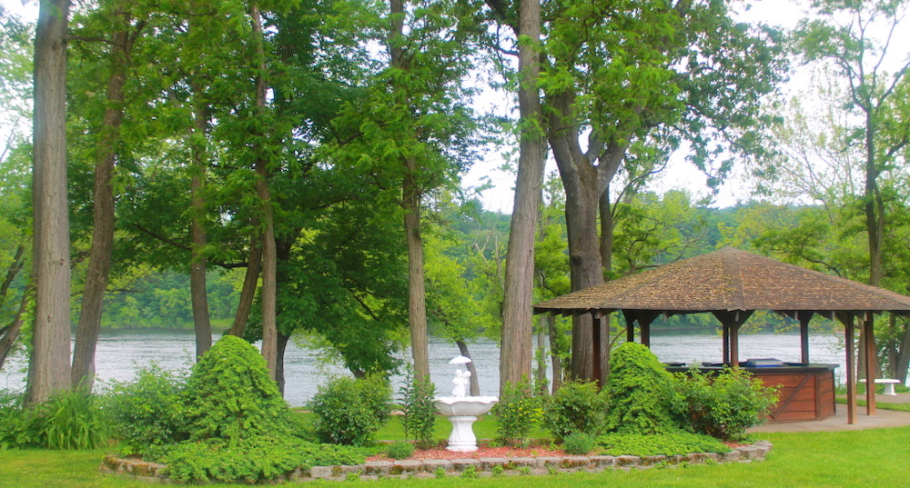 a tiki bar sits in a copse of trees near a lake