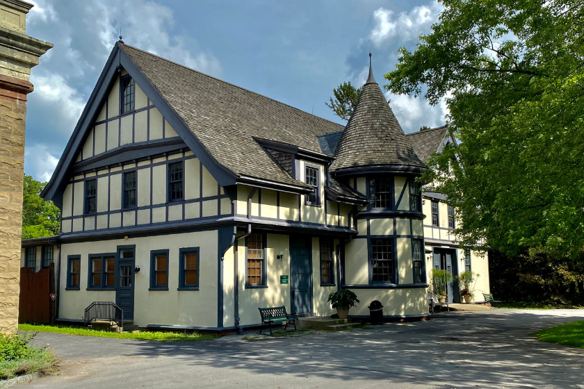 house with prominent tent-roofed turret, half-timbered stucco fa&ccedil;ade, and the prominent bargeboards on the gables, the Carriage House at Sonnenberg Gardens State Historic Park.