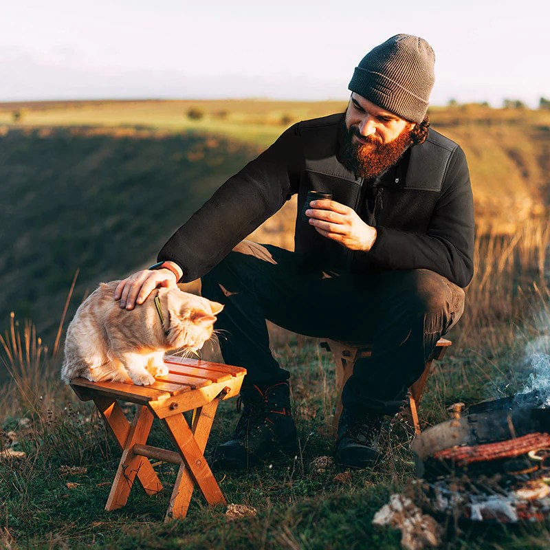 Person petting a cat on a table in a field while wearing a Tidewe jacket