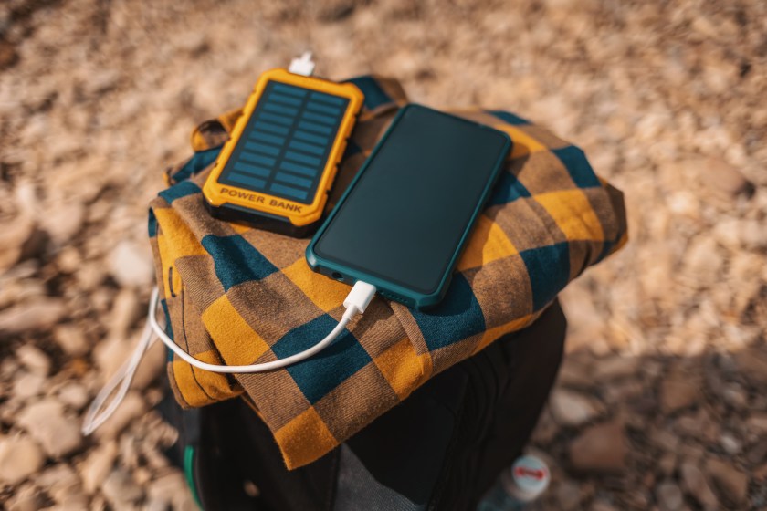 Solar power bank charges the smartphone via a USB cable. Top view, close-up. Pebble on the background. Soft focus. Concept of modern gadgets and renewable energy.