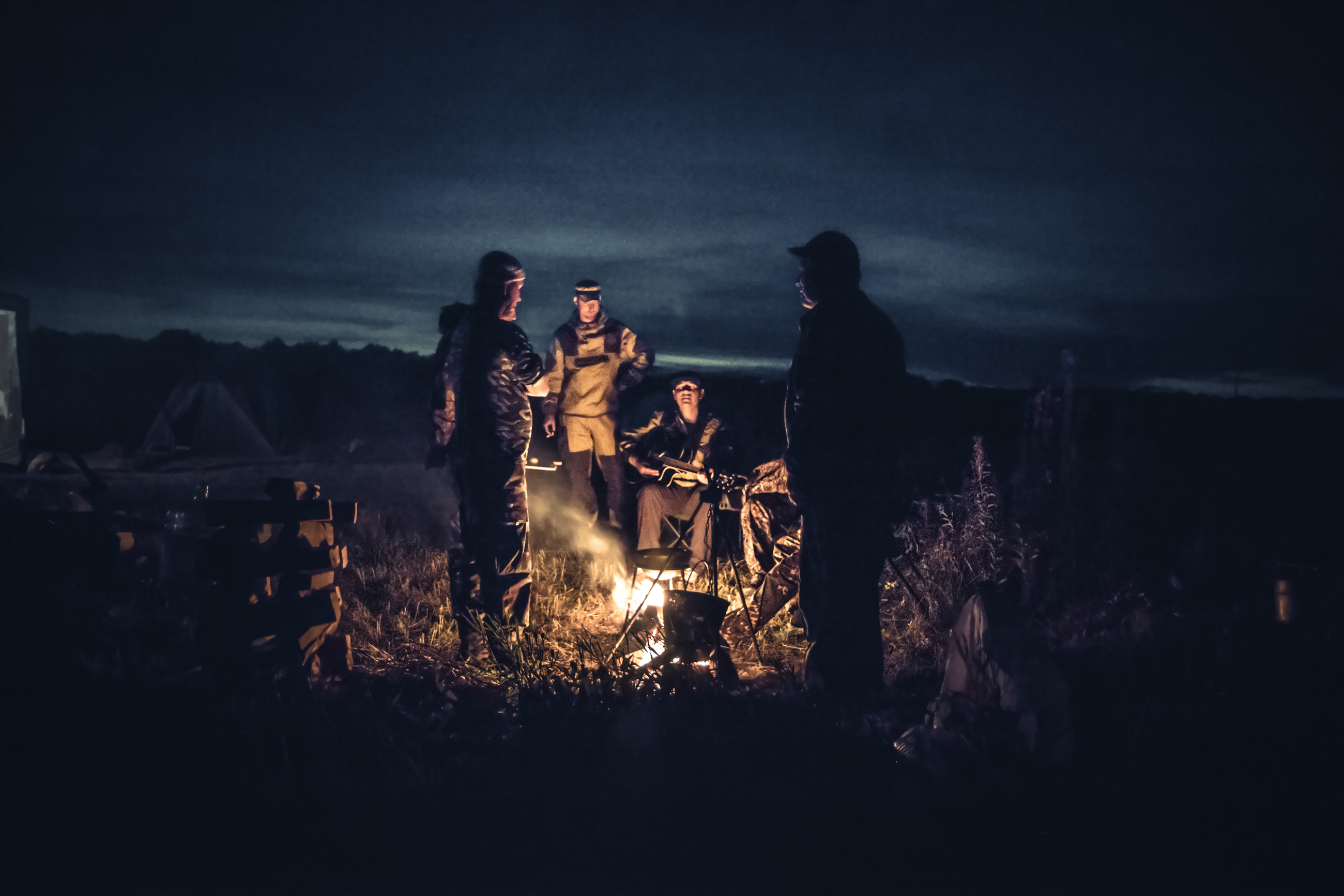 Group of men people travelers tourist resting campfire in outdoors camp after long hunting day in the night