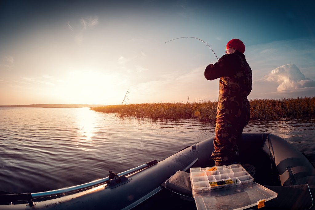 Man fishing from the boat on the lake at sunset