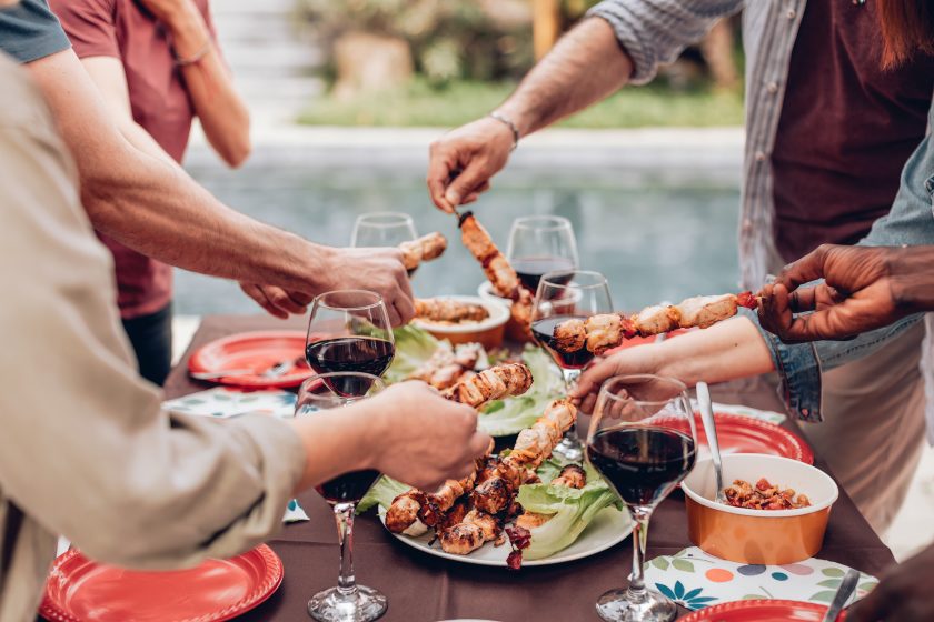 hands grabbing skewers from the table with wine glasses at the poolside summer barbecue party