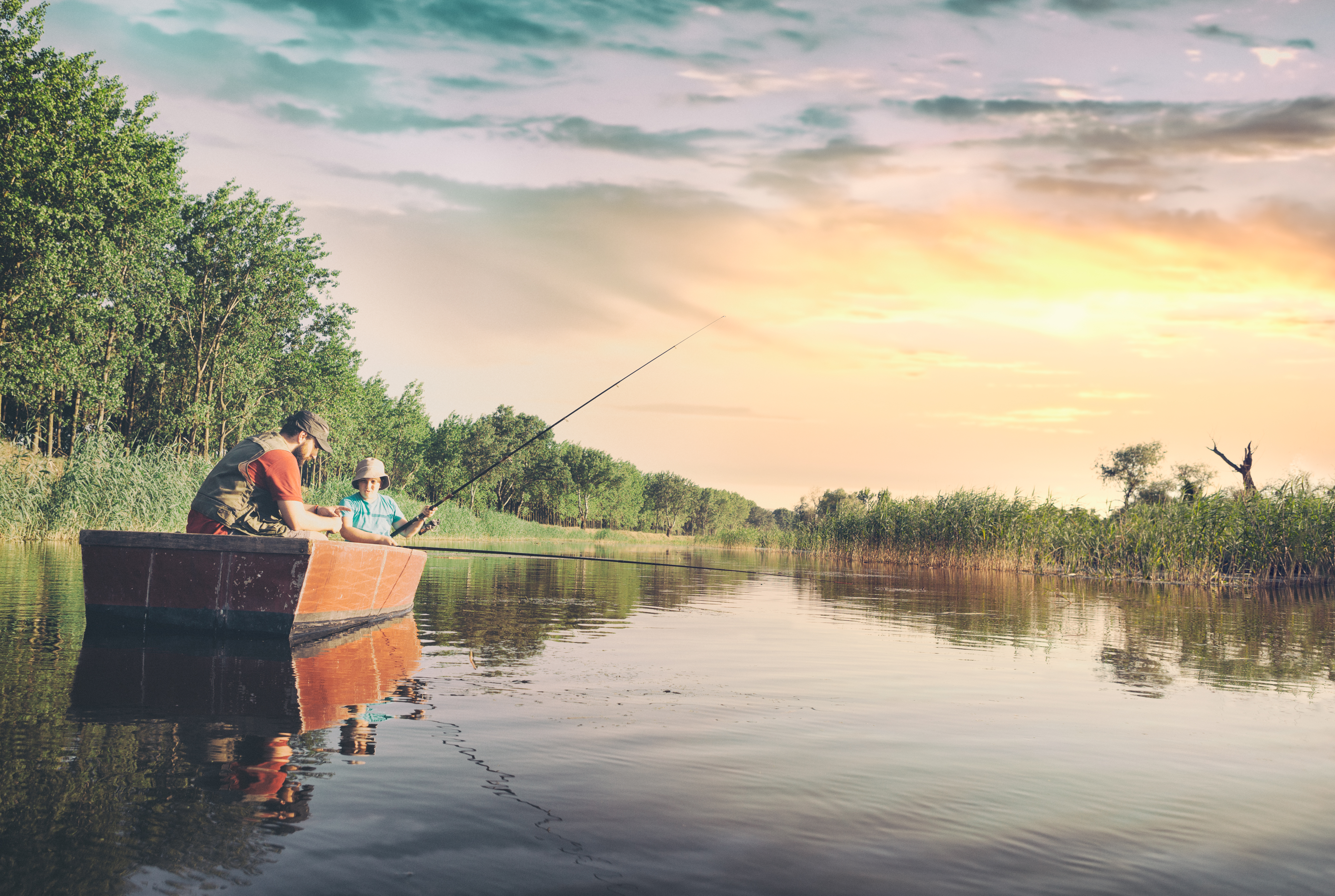 Dad and son sitting in boat and fishing on lake, the boy showing his dad how he caught a fish