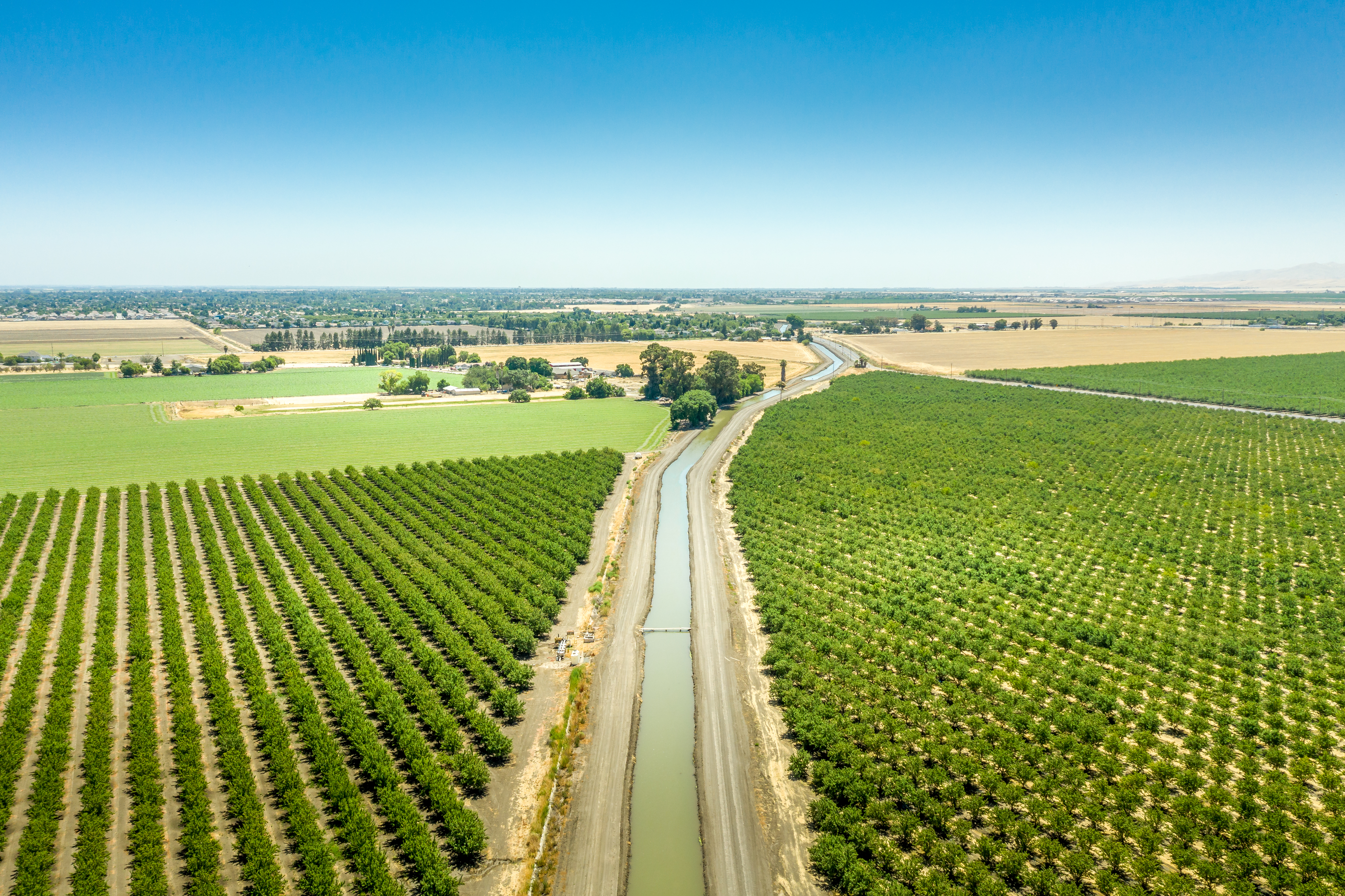 Aerial View of California Aqueduct winding its way through crops and open farm land. Blue sky and green and gold frm land below.