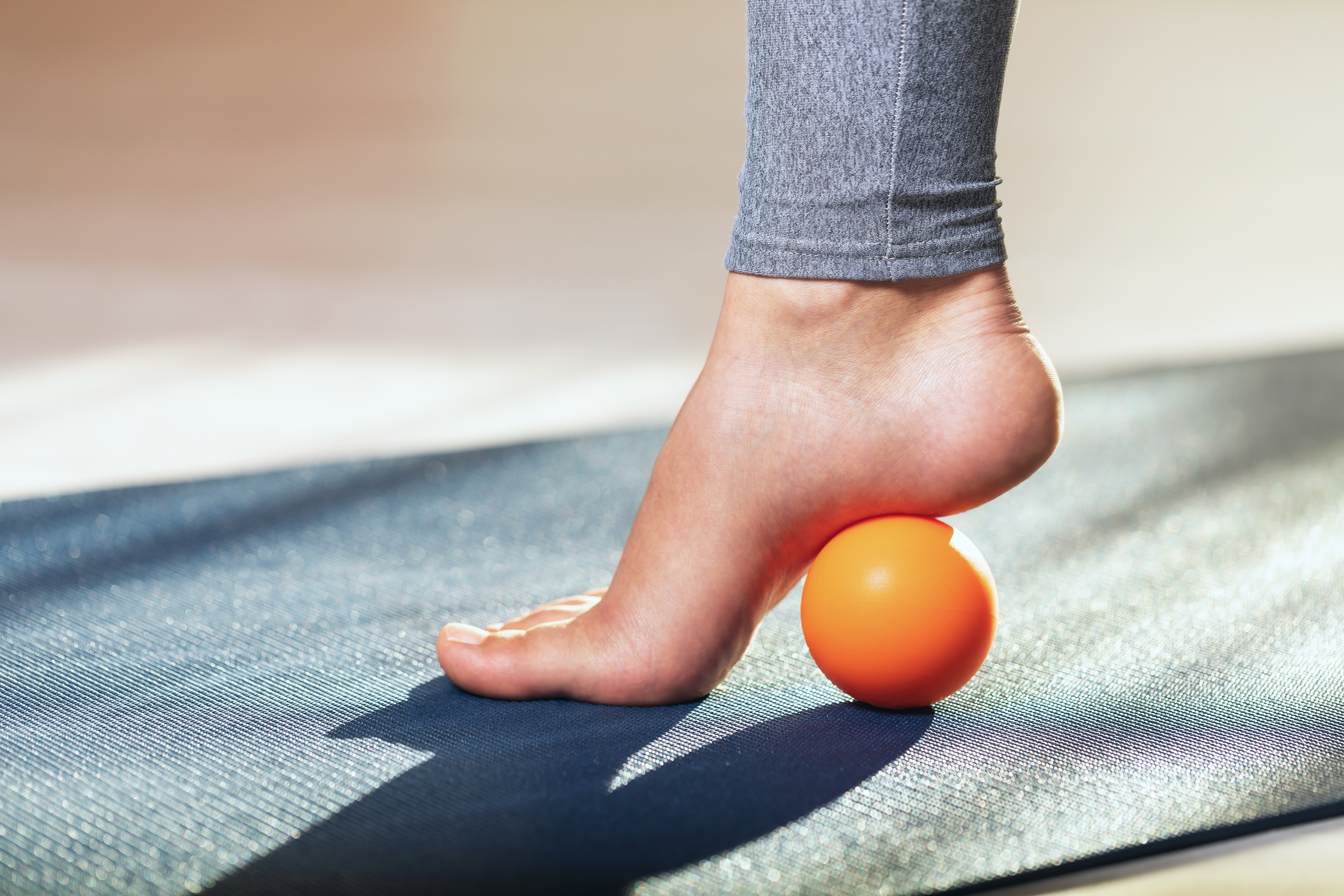 Myofascial release of hyper-movable muscles of the foot with a massage ball on a gymnastic mat at home. Prevention of leg fatigue after wearing high heel shoes.
