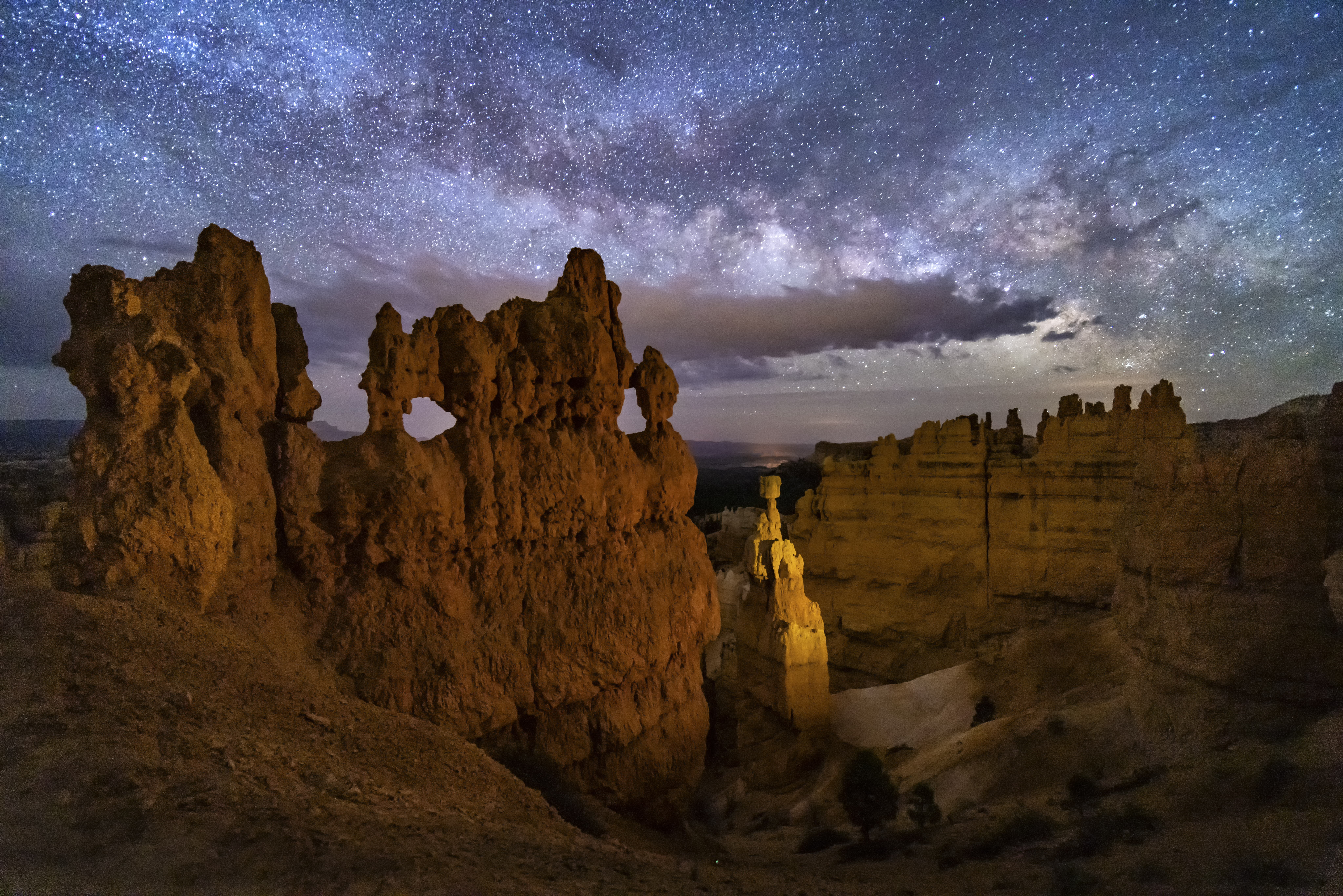 A hoodoo with small windows and Thor's Hammer against a night sky with clouds and the Milky Way below Sunset Point in bryce Canyon National Park, Utah.