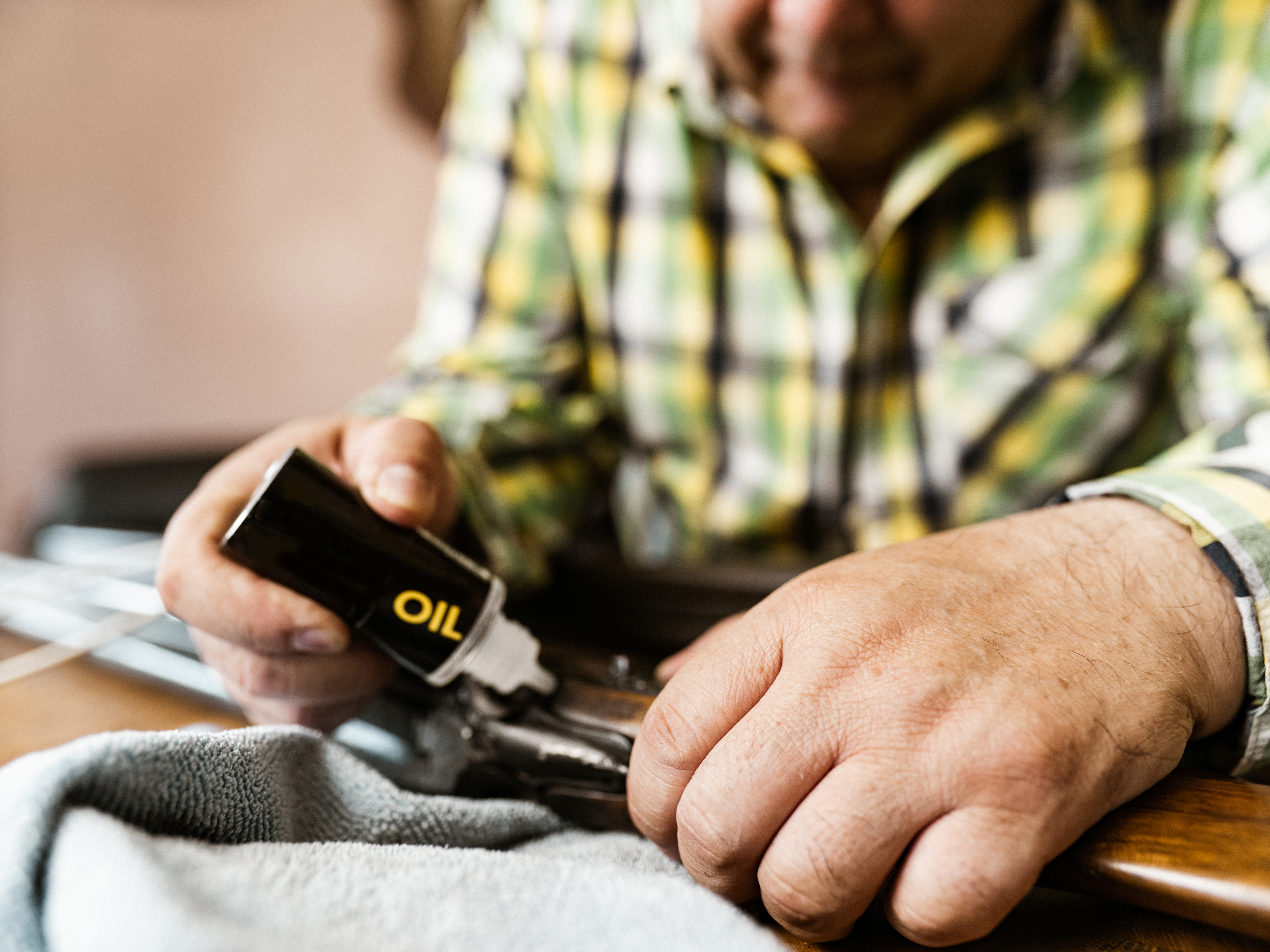 Hands close up of Mature Latin man of Mexican heritage cleaning his hunting rifle. He is wearing casual clothes with plaid shirt. Interior of private home.