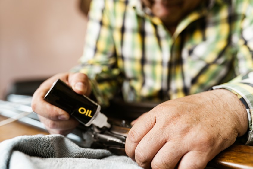 Hands close up of Mature Latin man of Mexican heritage cleaning his hunting rifle. He is wearing casual clothes with plaid shirt. Interior of private home.