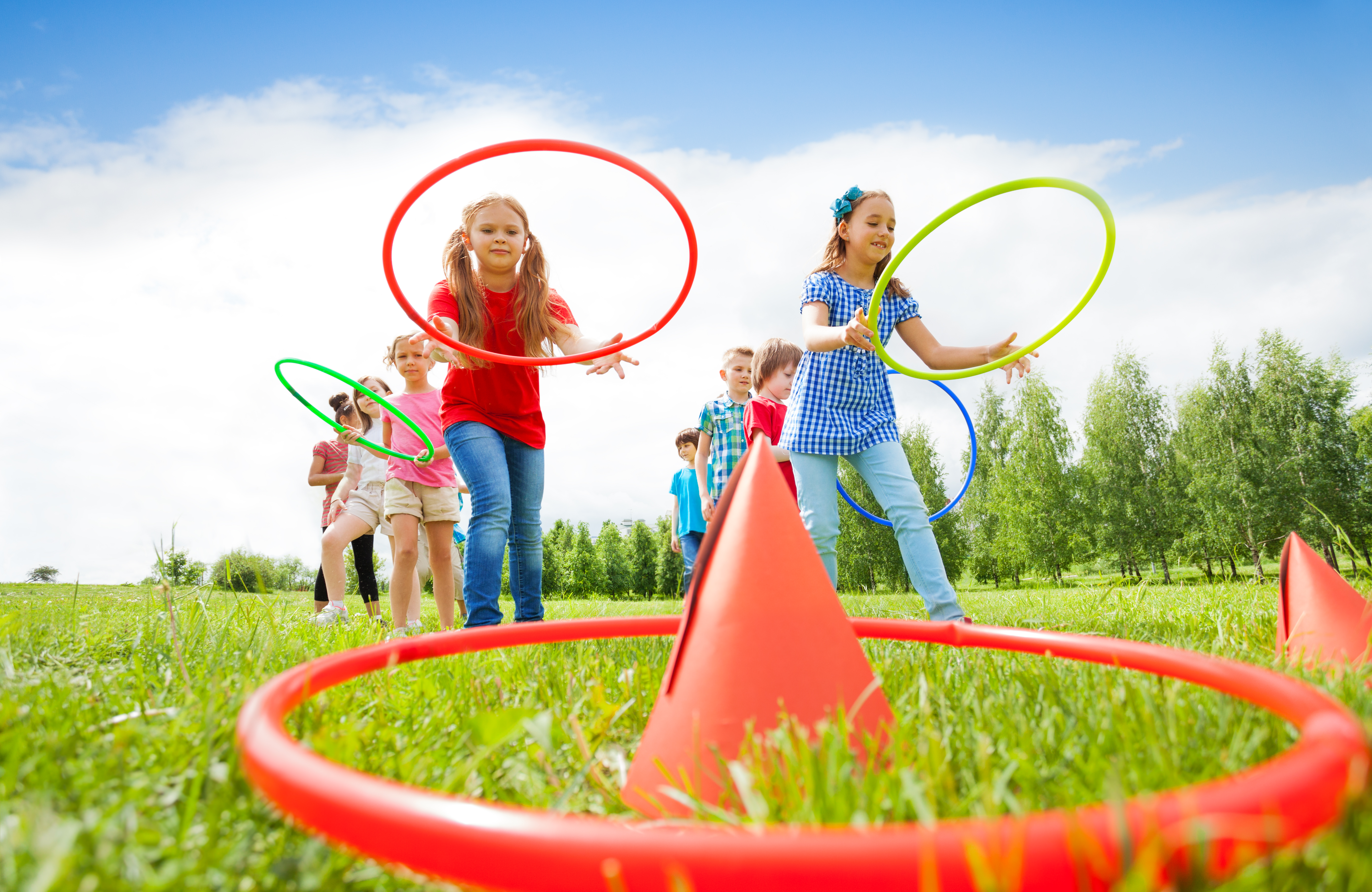 Two group of kids playing with colorful hoops and throw them on cones while competing with each other during summer sunny day