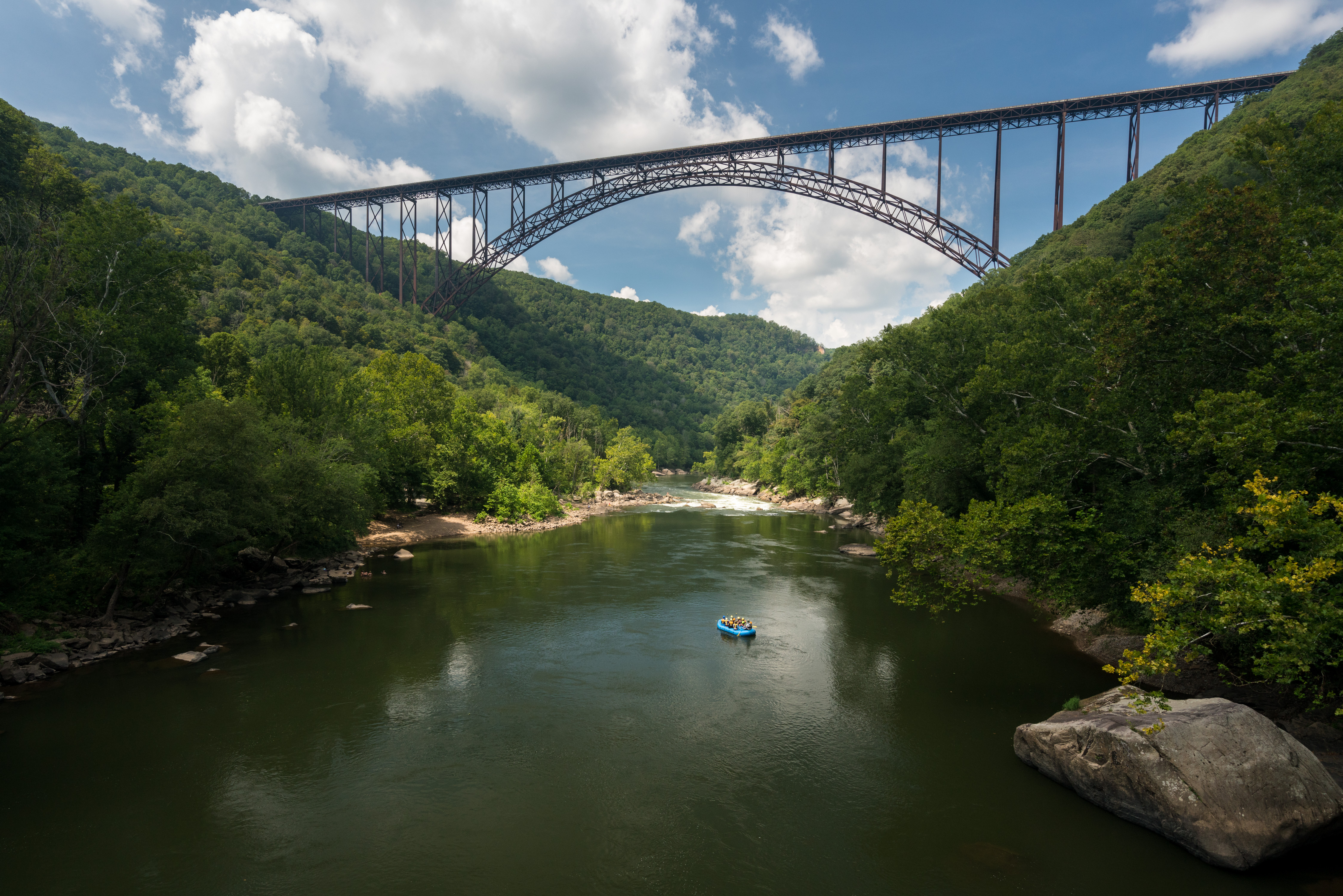 Rafters float towards the rapids under the high arched New River Gorge bridge in West Virginia 