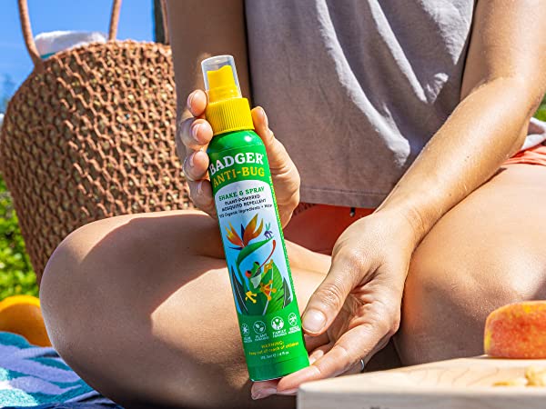 Person sitting down in the grass, holding a bottle of Badger Anti-Bug Shake & Spray Mosquito Repellent 