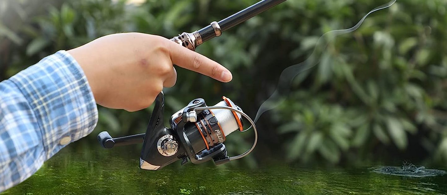 Hang holding the bottom of a Eagle Hunting 9 Telescopic Fishing Rod with a finger pointing out onto a green body of water