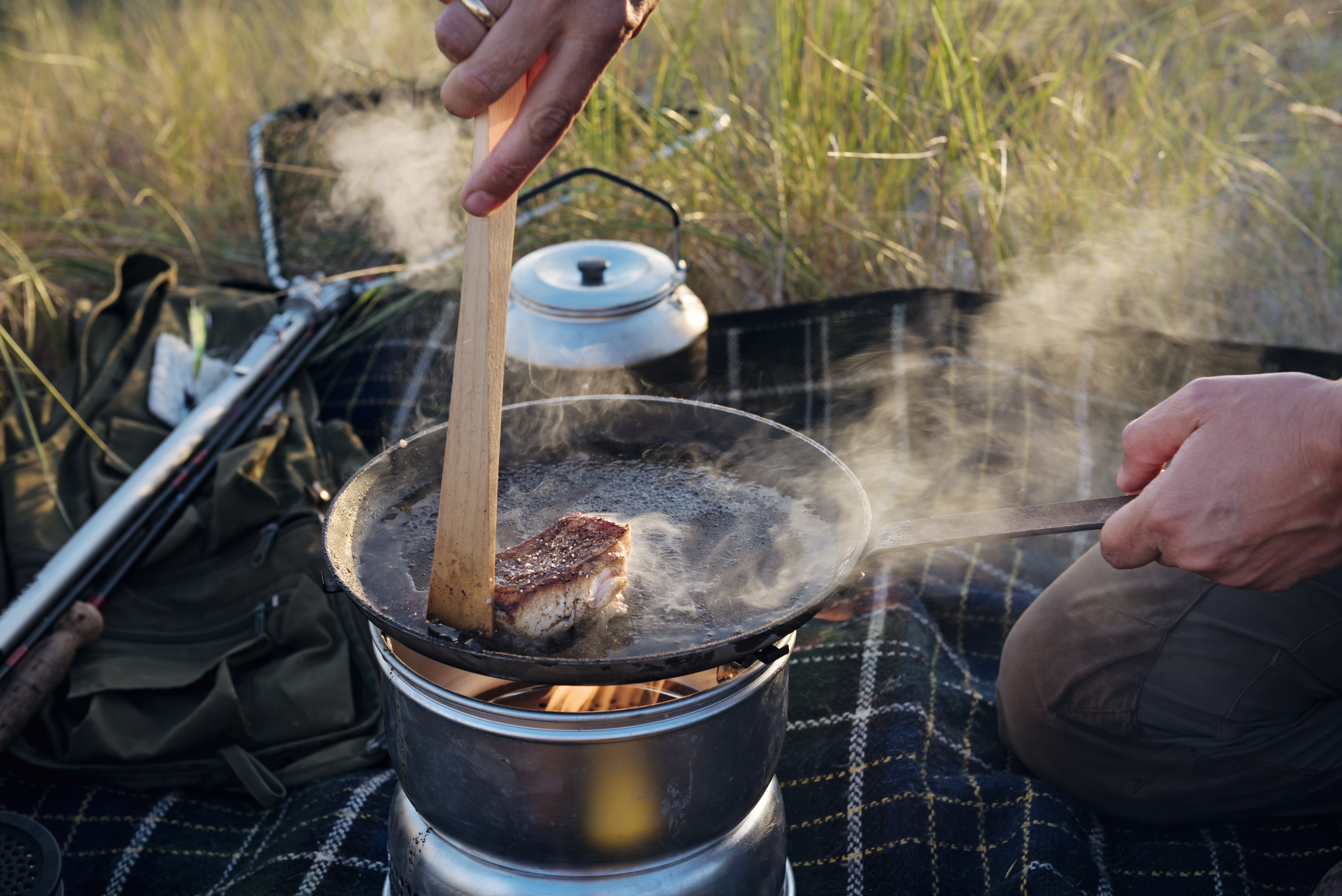 Fisherman cooking her catch at the beach. Female fisherman preparing a filled piece of fish she caught earlier. She is using a gas camping stove in a sheltered spot in the dunes next to the beach where she was fishing. Colour horizontal with some copy space. Shot on location on the island of M&oslash;n in Denmark.