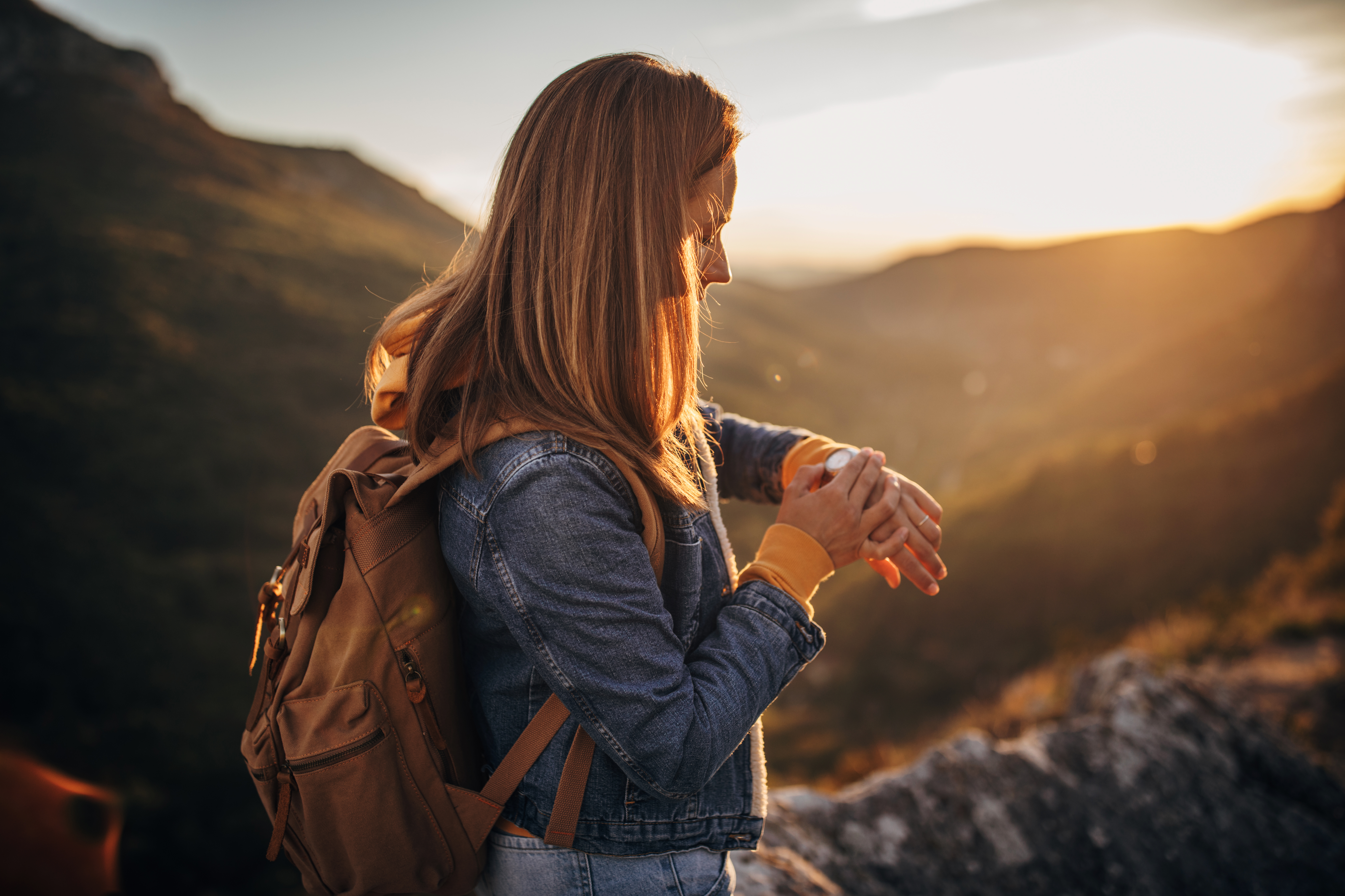One beautiful young woman standing on the top of a mountain and checking the time on wristwatch.