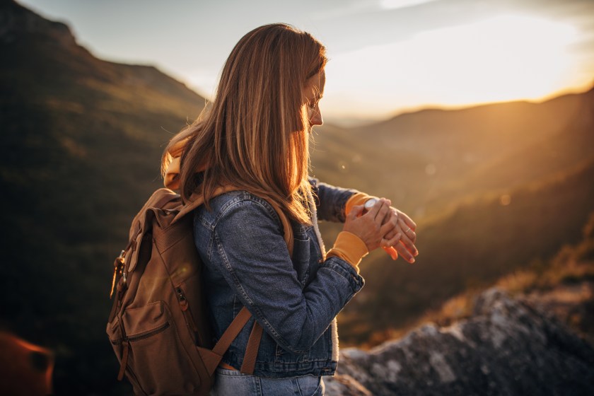 One beautiful young woman standing on the top of a mountain and checking the time on wristwatch.
