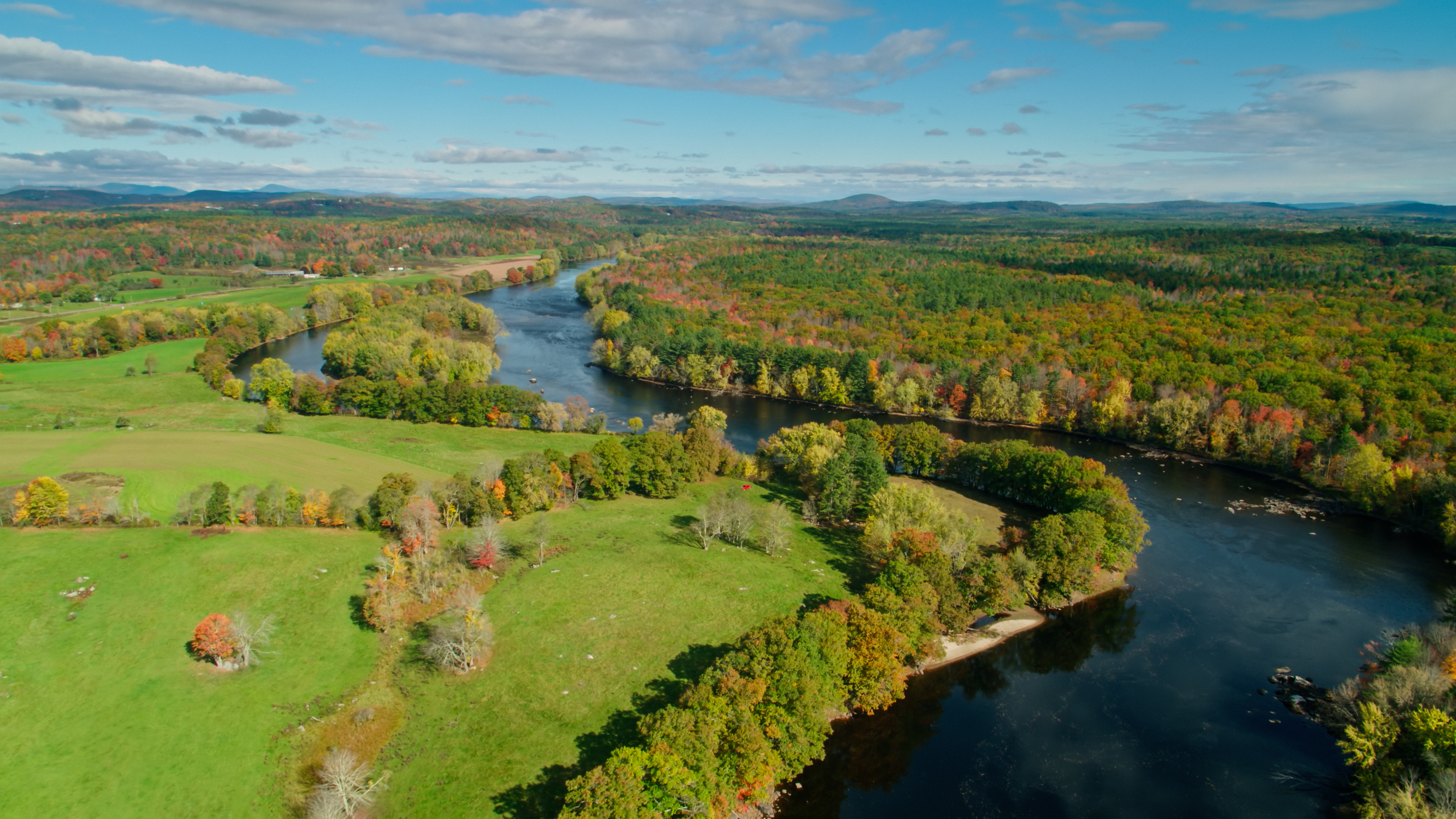 Aerial shot of Androscoggin River flowing past forest and farmland near Turner, Maine on a clear sunny day in autumn.