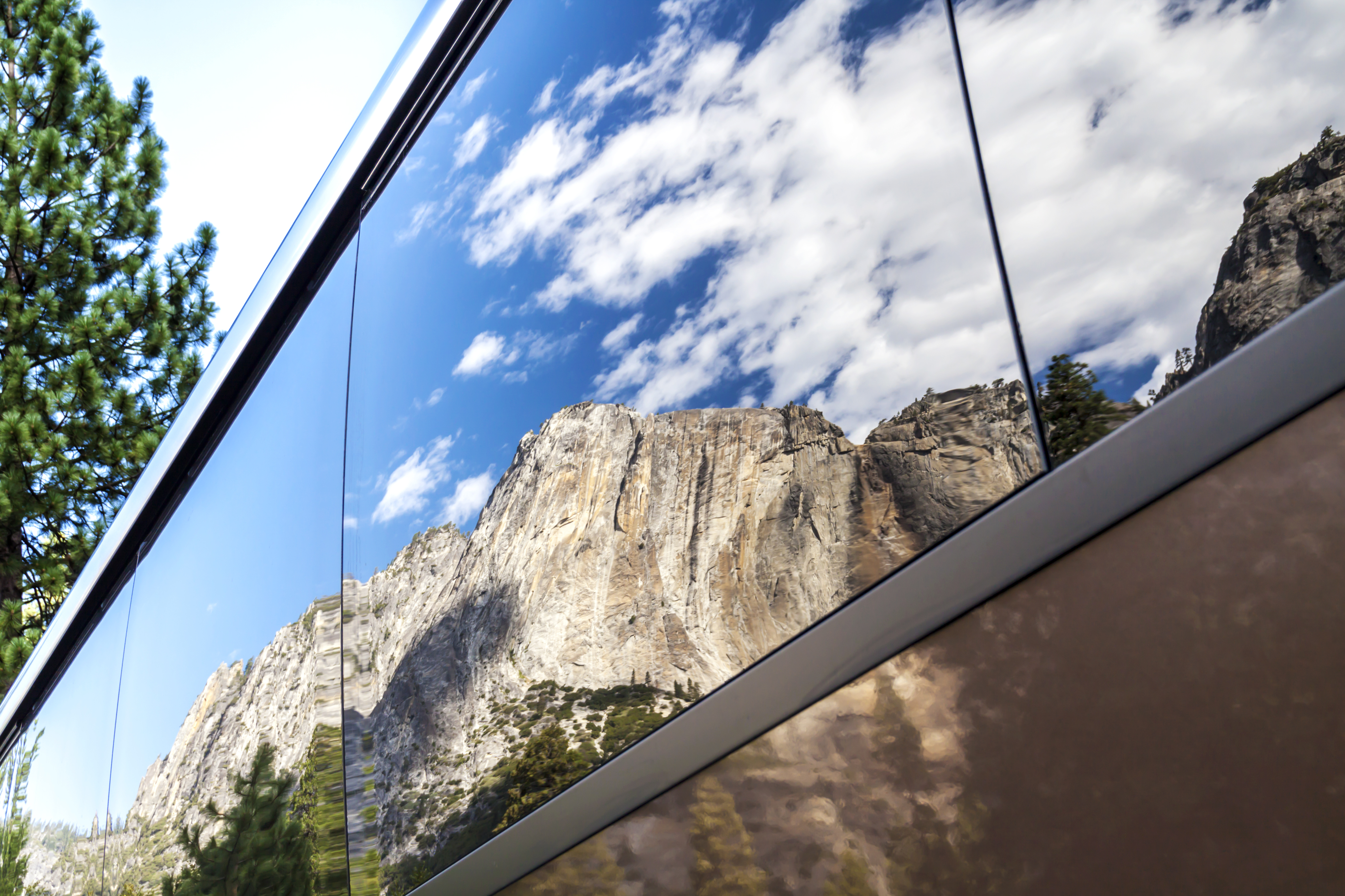 The vertical rock formation of El Capitan in Yosemite National Park, reflected in the tinted glass windows of a tourist bus. 