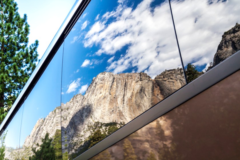 The vertical rock formation of El Capitan in Yosemite National Park, reflected in the tinted glass windows of a tourist bus.