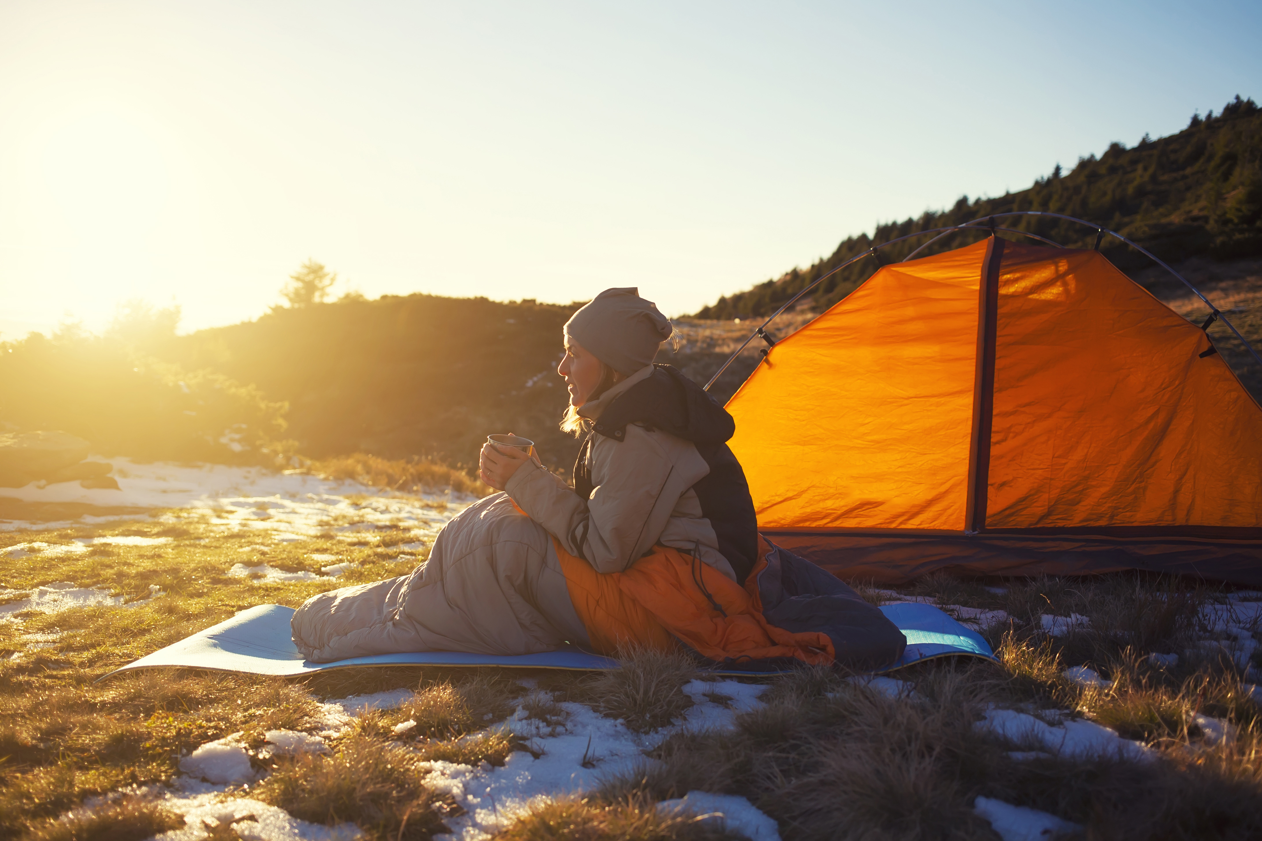 Girl sitting in a sleeping bag and drinking hot drink.