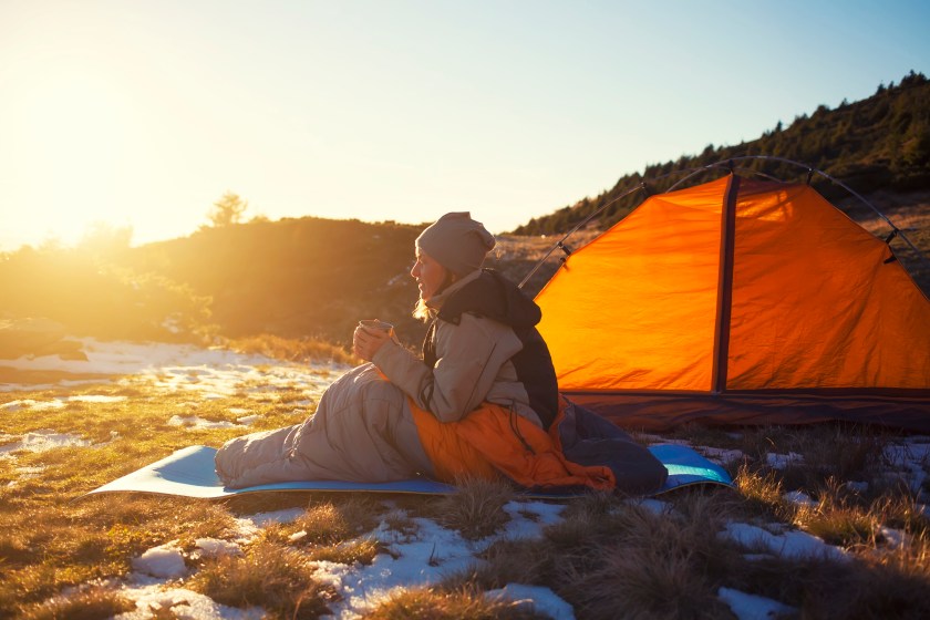Girl sitting in a sleeping bag and drinking hot drink.