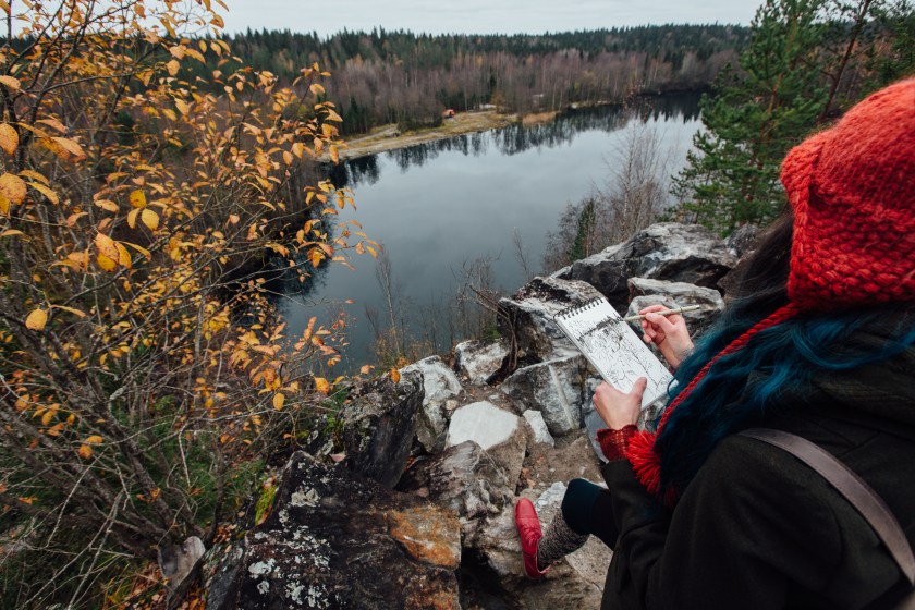 Artist painting while sitting on the rocks at the cliff.