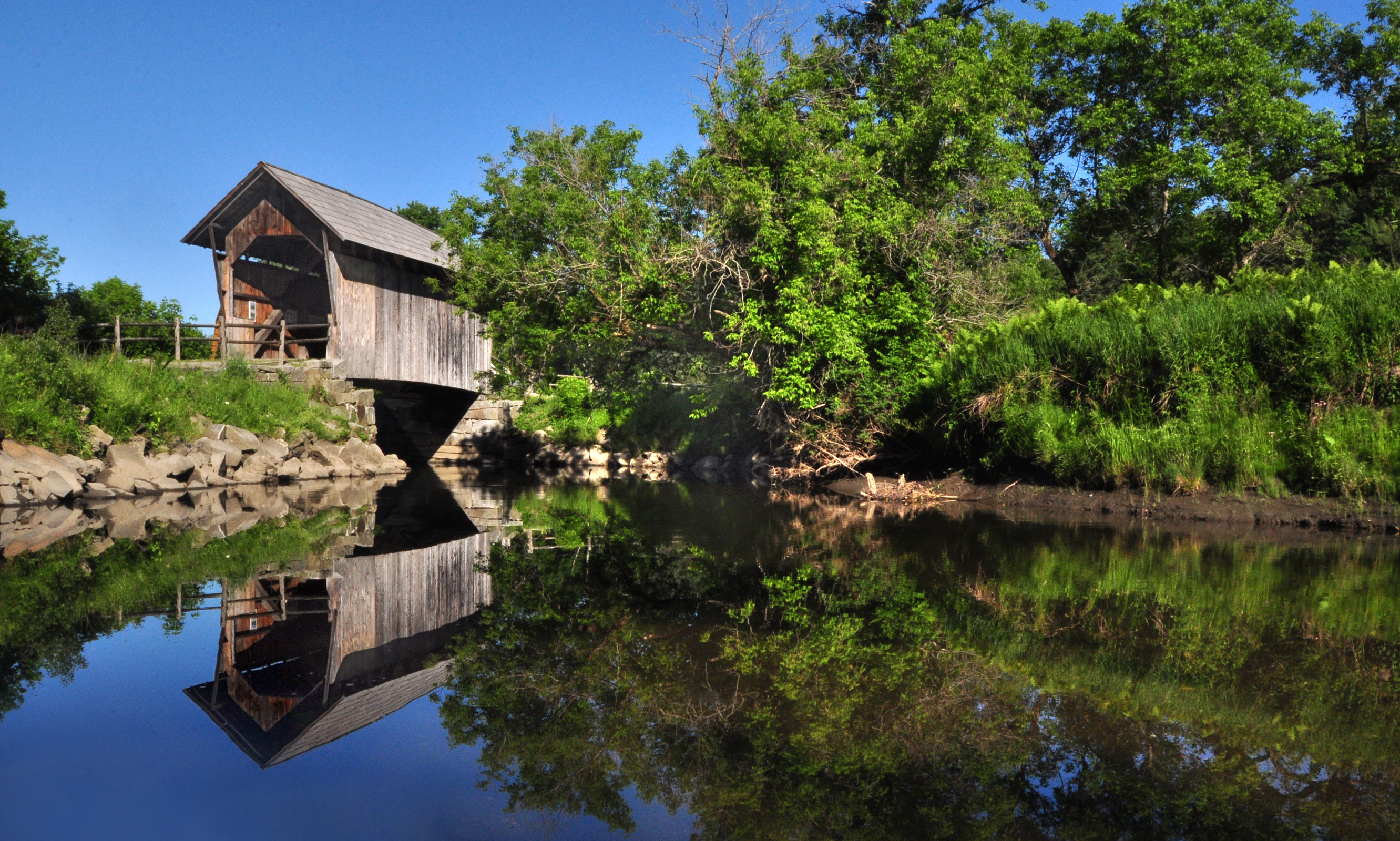 A covered bridge crosses the Winooski River in a pasture.