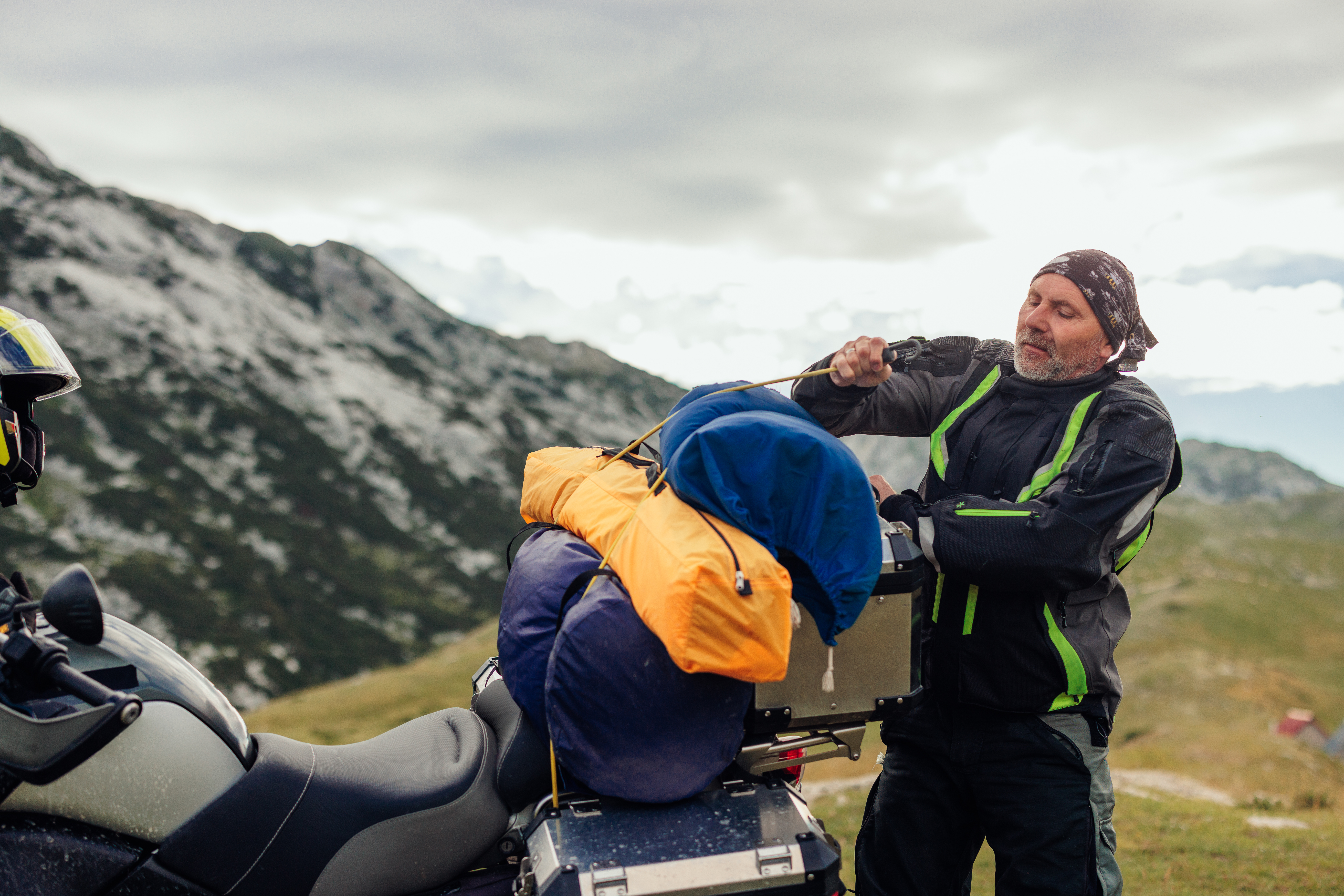 Mature biker has assembled his camping gear and is packing and strapping it onto his bike's panniers.