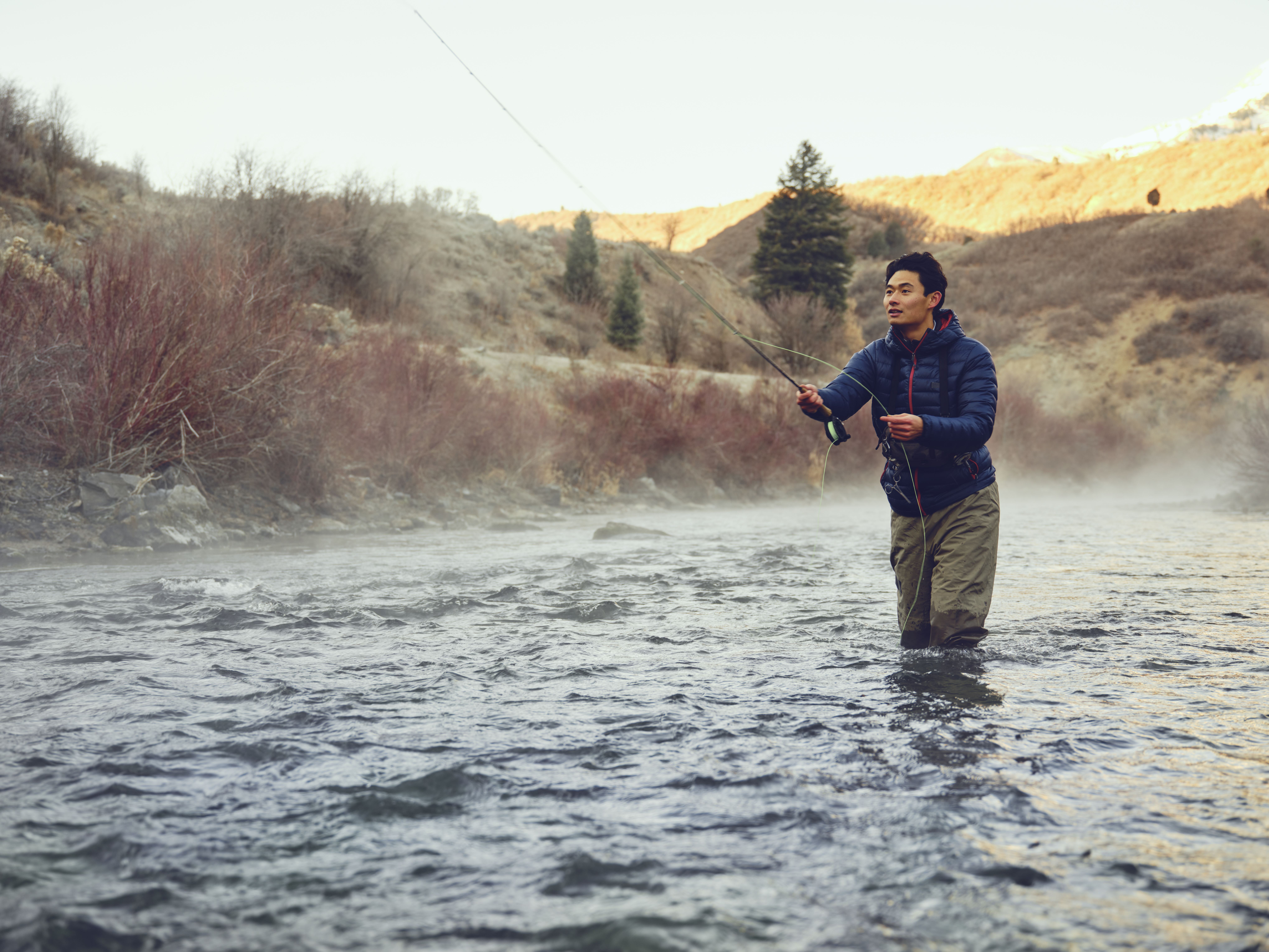 An Asian Korean man, fly fishing on the Provo River in Utah during winter.