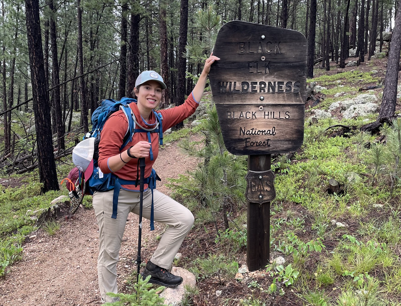 Hiker wearing a red rainjacket and khaki rain pants while on a hiking trail