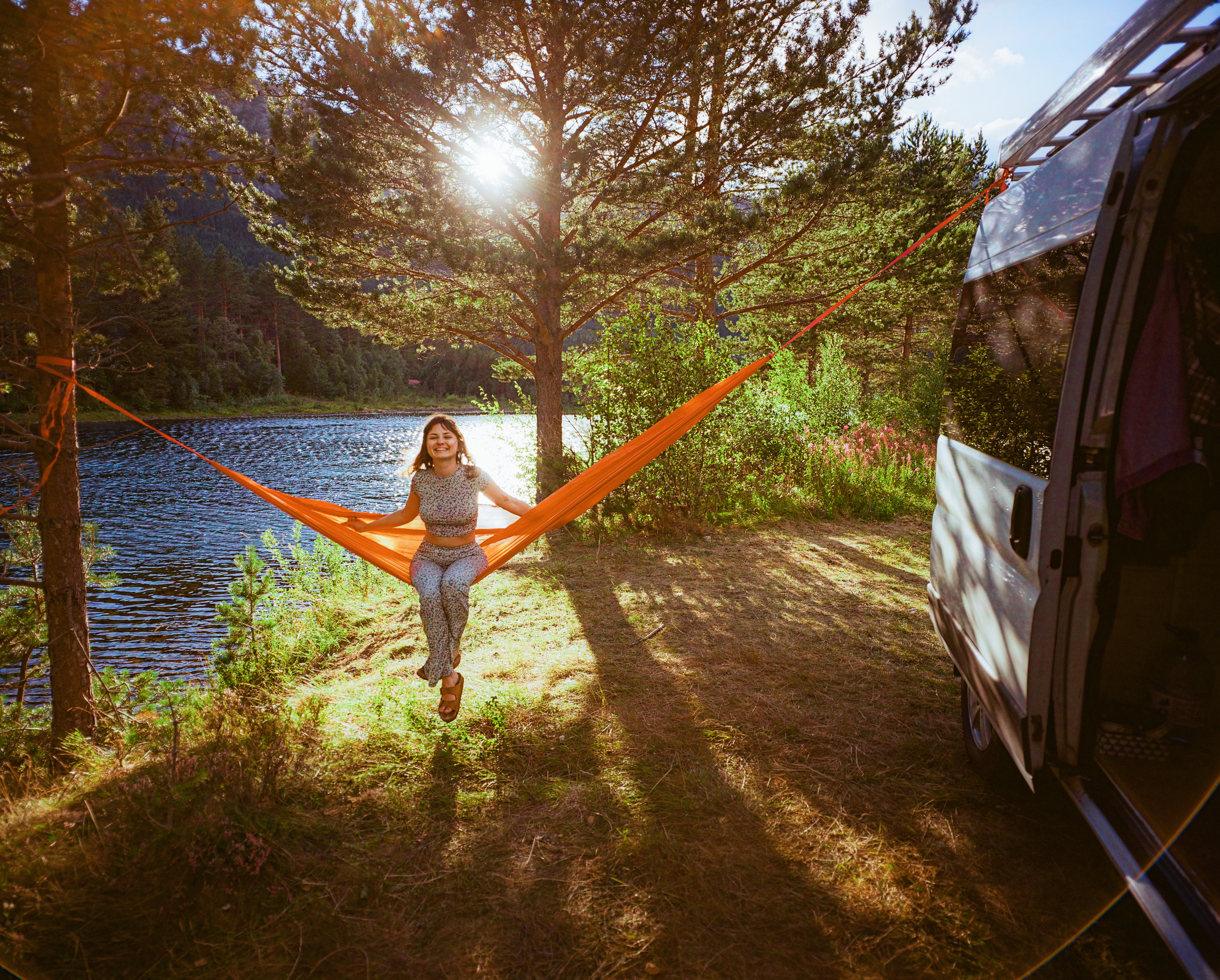 Young Caucasian woman resting in hammock near camper van in forest.