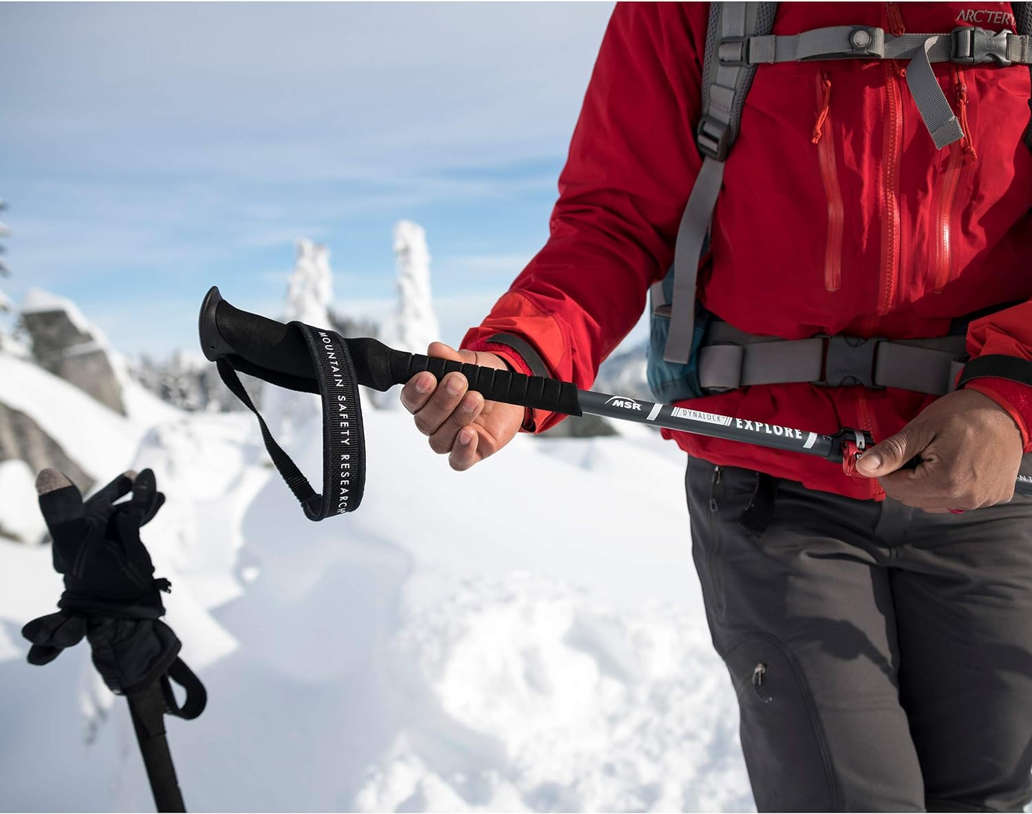 Person in red jacket holding red and black trekking poles in the snow