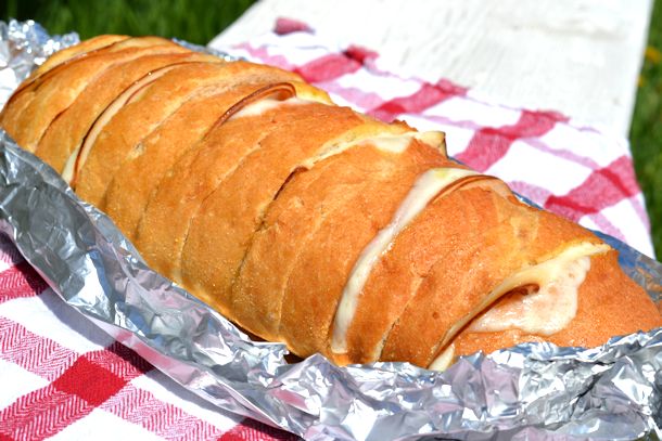 A ham and cheese pull apart bread in a foil bowl on a checkerboard tablecloth