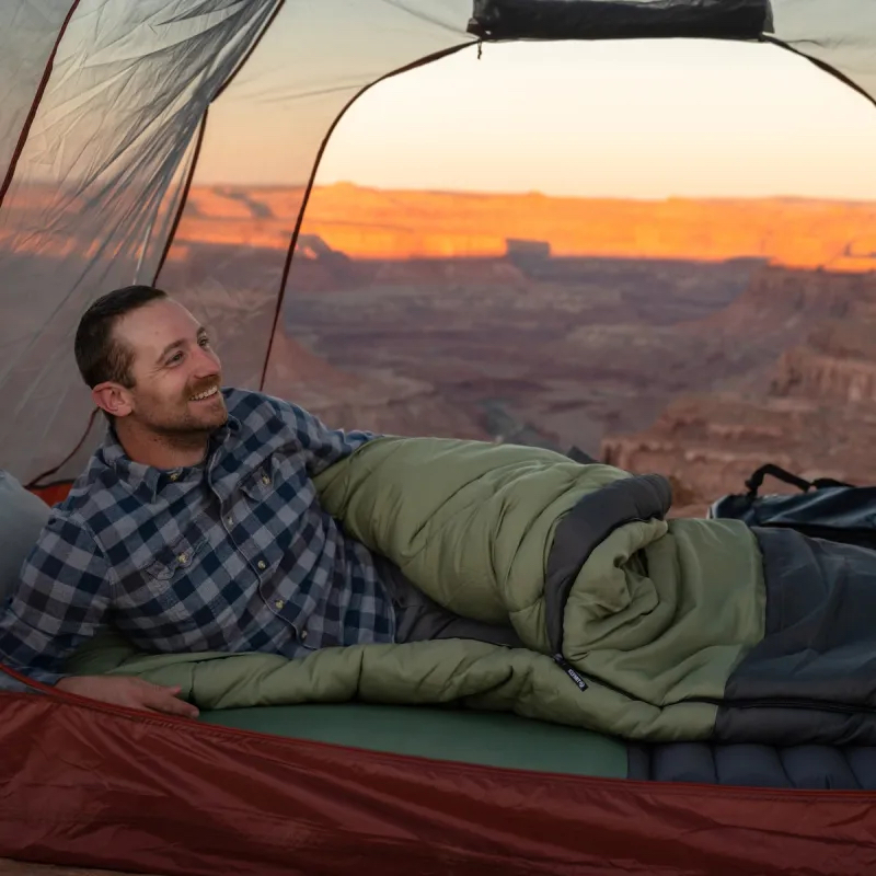 A person inside a camping tent sleeping with a green sleeping bag