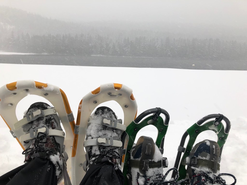 Mom and son snow shoeing at lake take a rest.