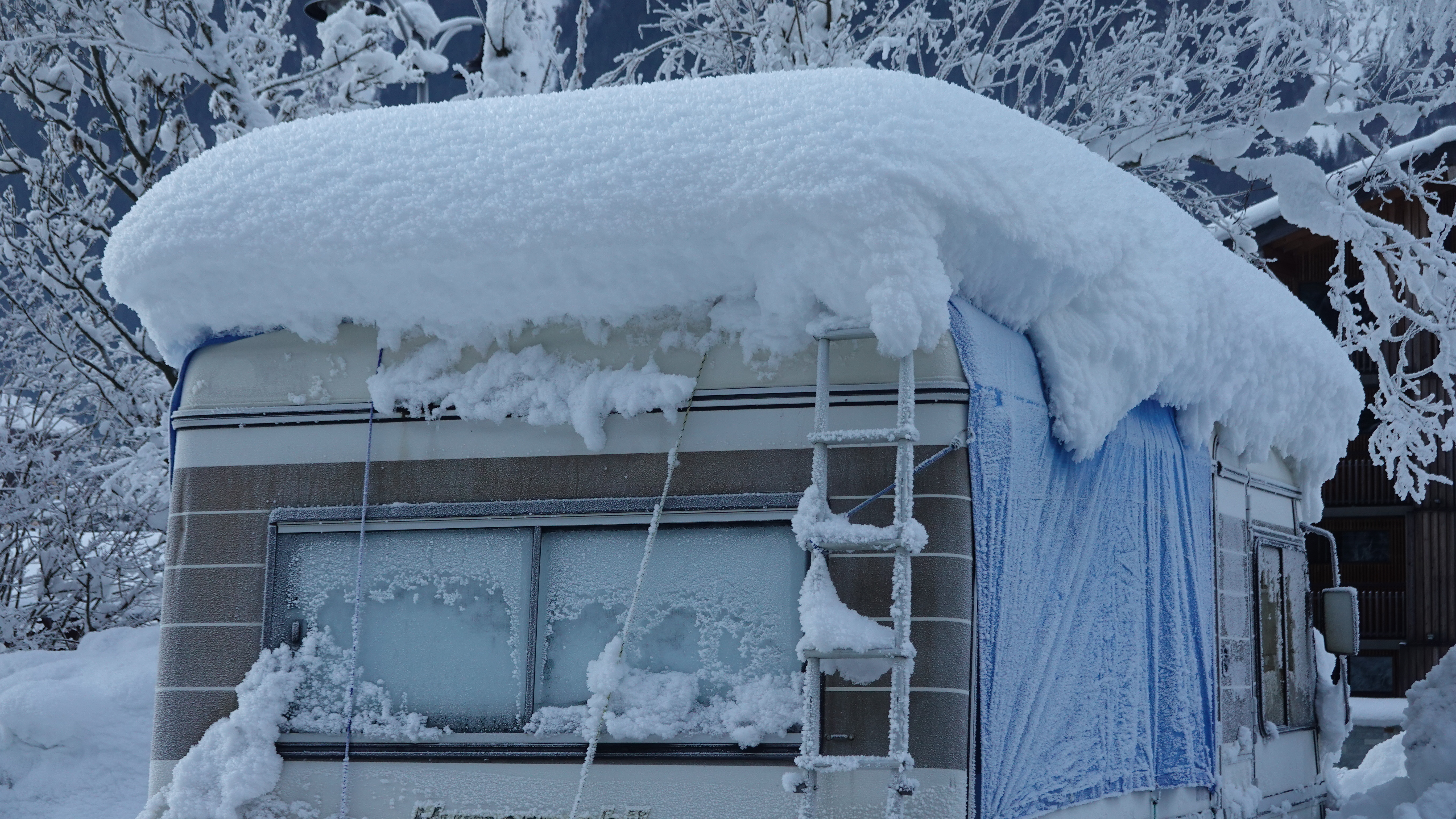 A trailer house covered in snow at a mountainous landscape