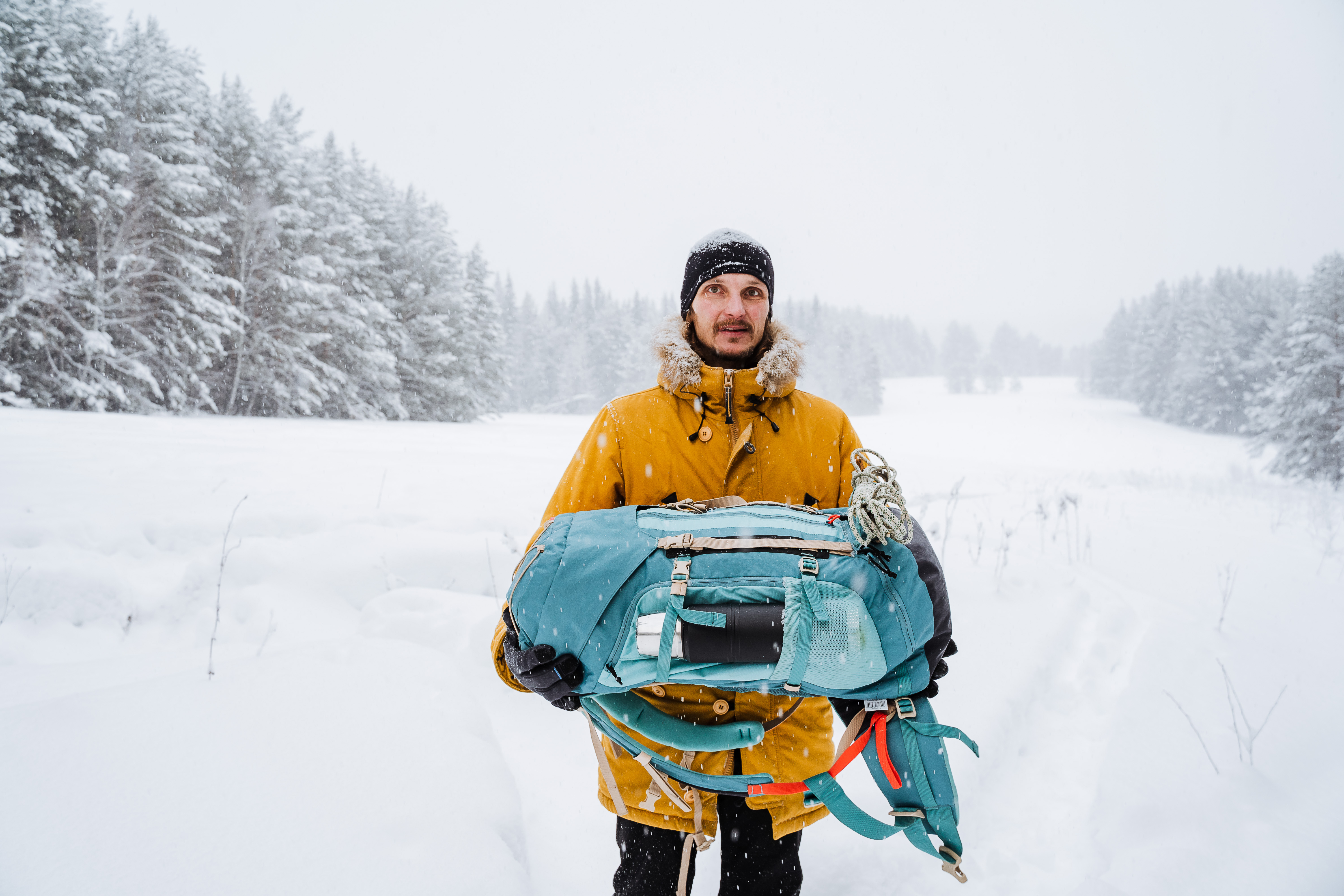 happy traveler carries a backpack in his hands. Bright hiking backpack with equipment,Snowy forest and rocks. Climbing the mountain in winter. Survival in the wild. High quality photo