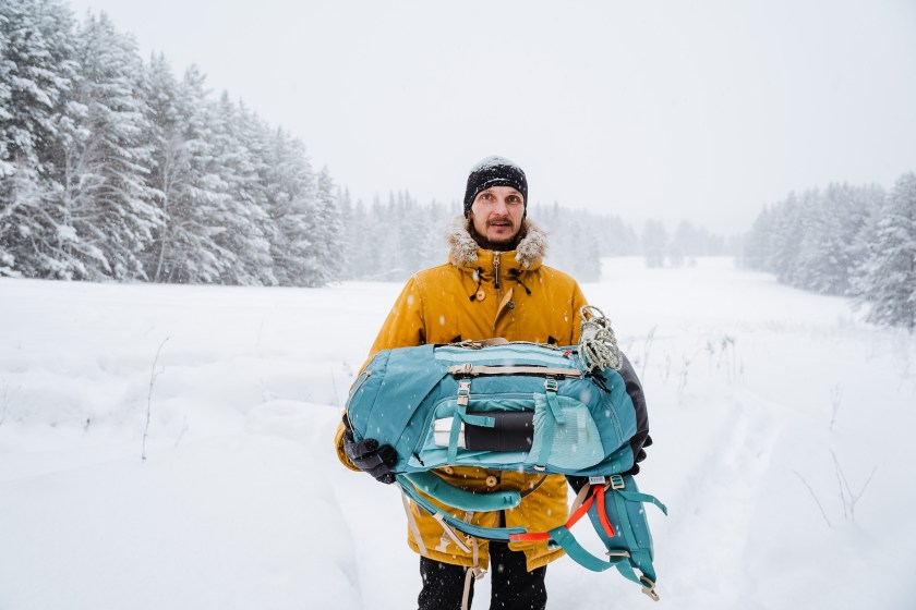 happy traveler carries a backpack in his hands. Bright hiking backpack with equipment,Snowy forest and rocks. Climbing the mountain in winter. Survival in the wild. High quality photo