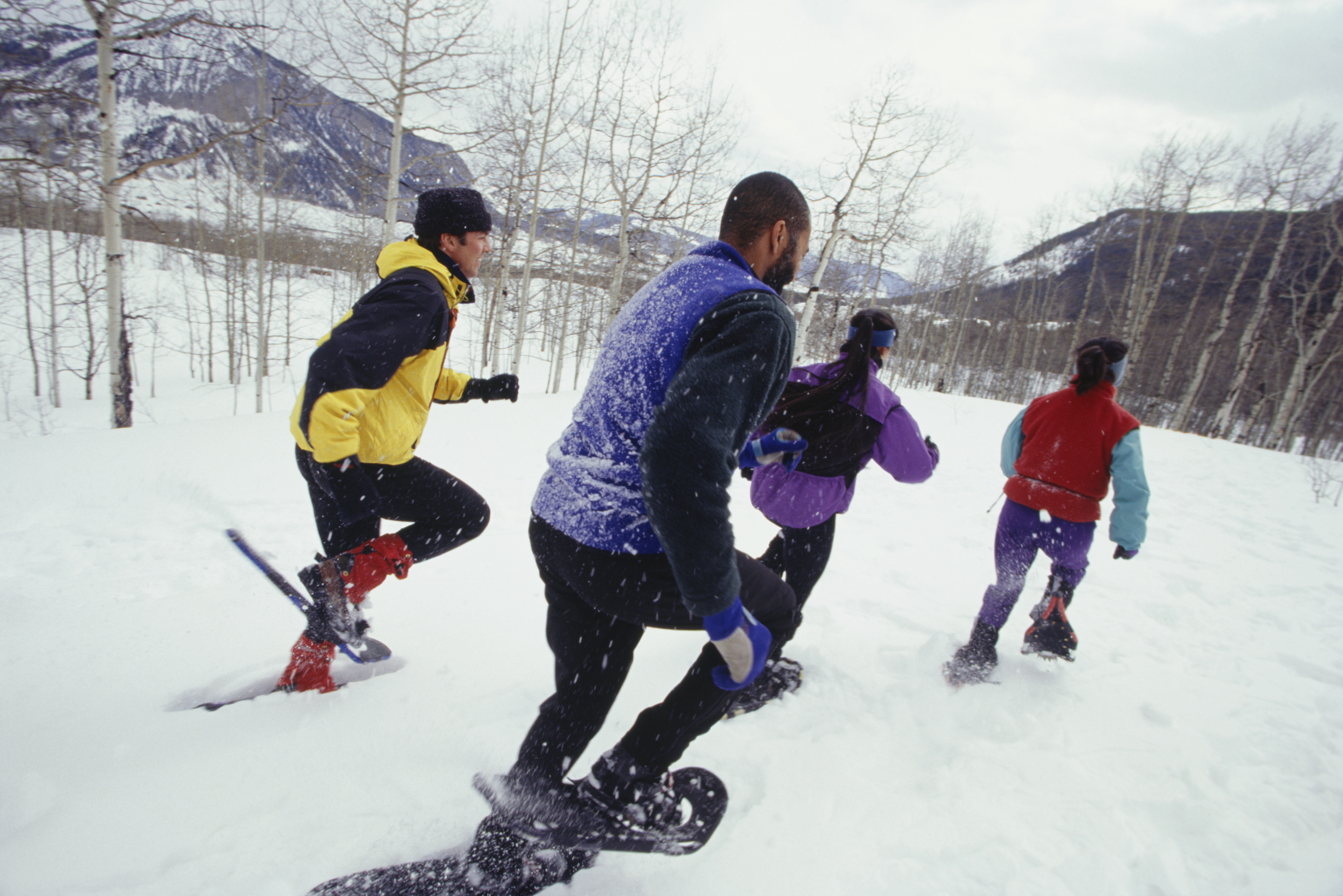 Four people wearing snowshoes walking up a snow-covered slope.