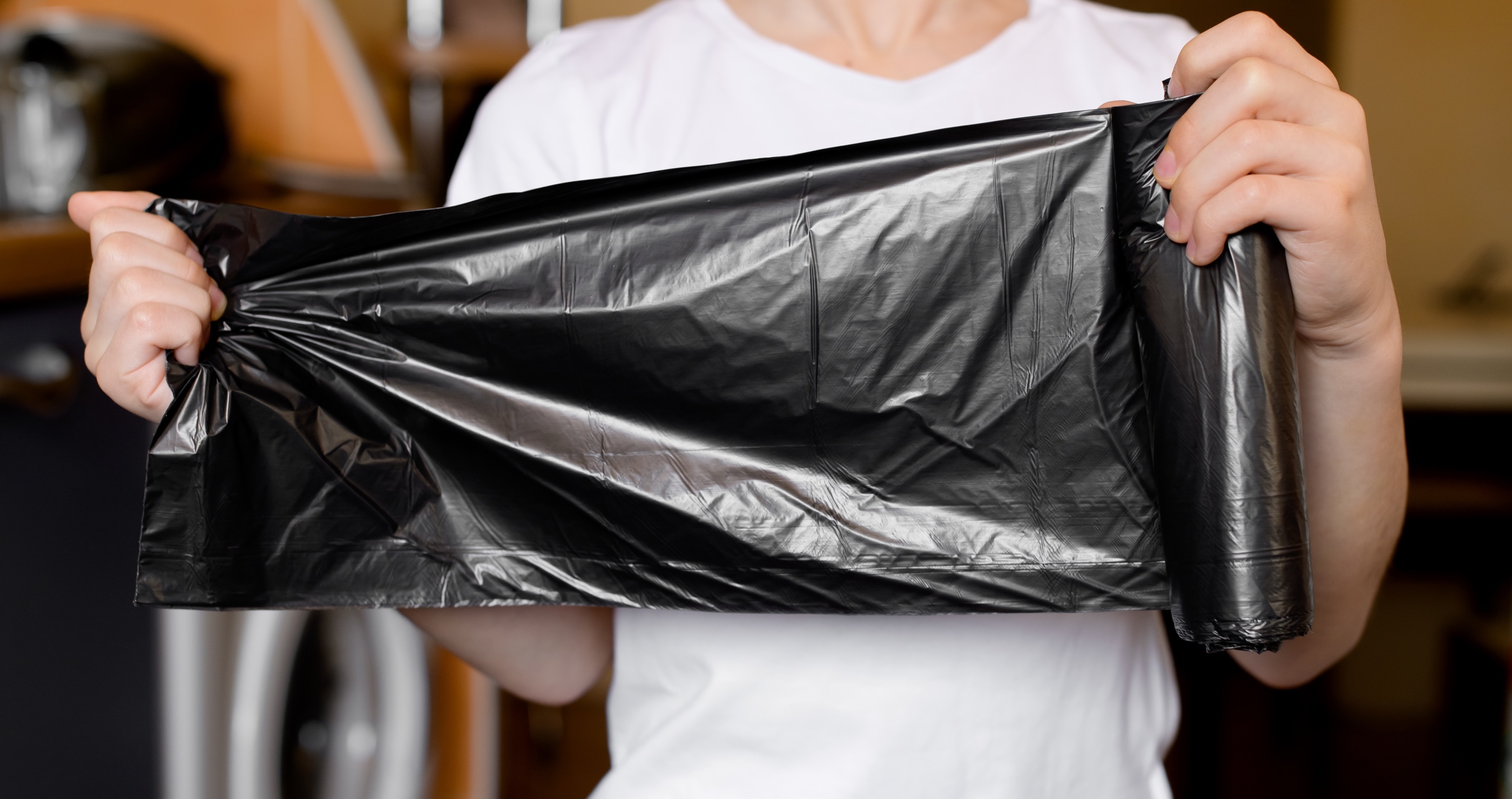 A woman stretching out a roll of black garbage bags