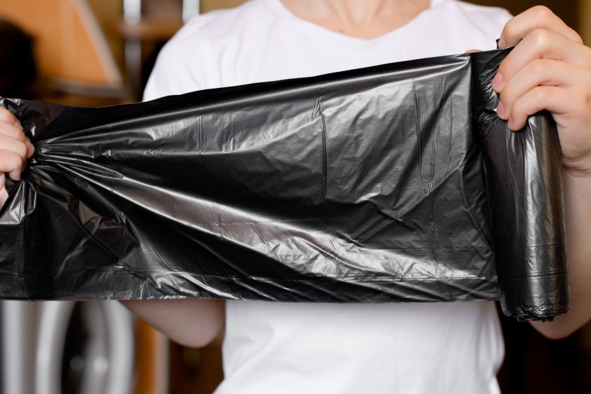 A woman stretching out a roll of black garbage bags